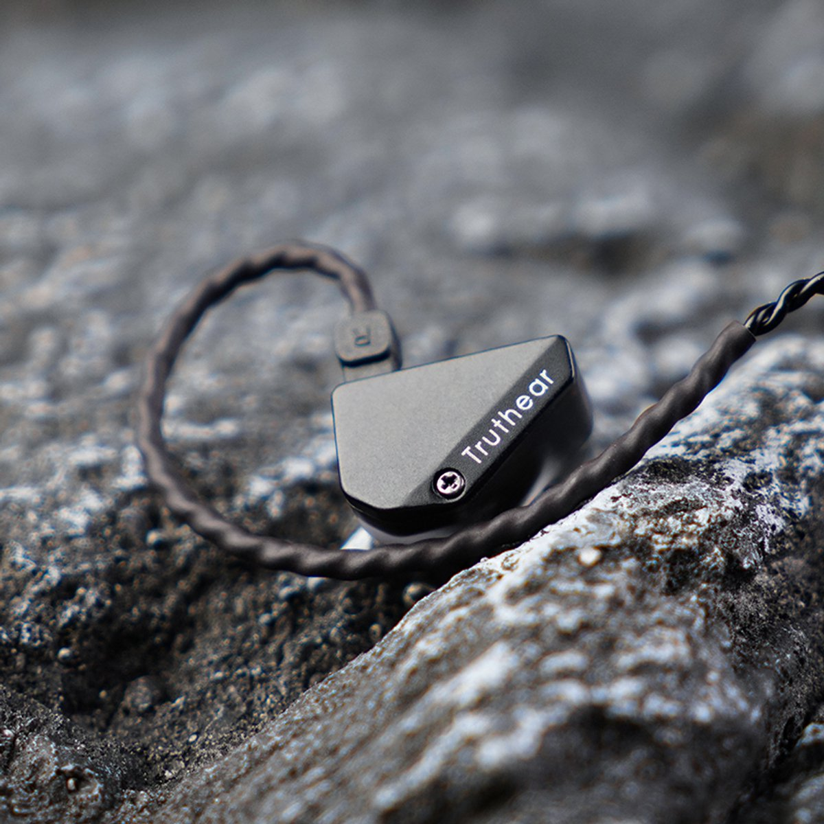 Nahaufnahme eines schwarzen In-Ear-Monitors auf einer grauen Felsfläche. Der Markenname 'Truthear' ist sichtbar. Das Kabel ist verdreht.