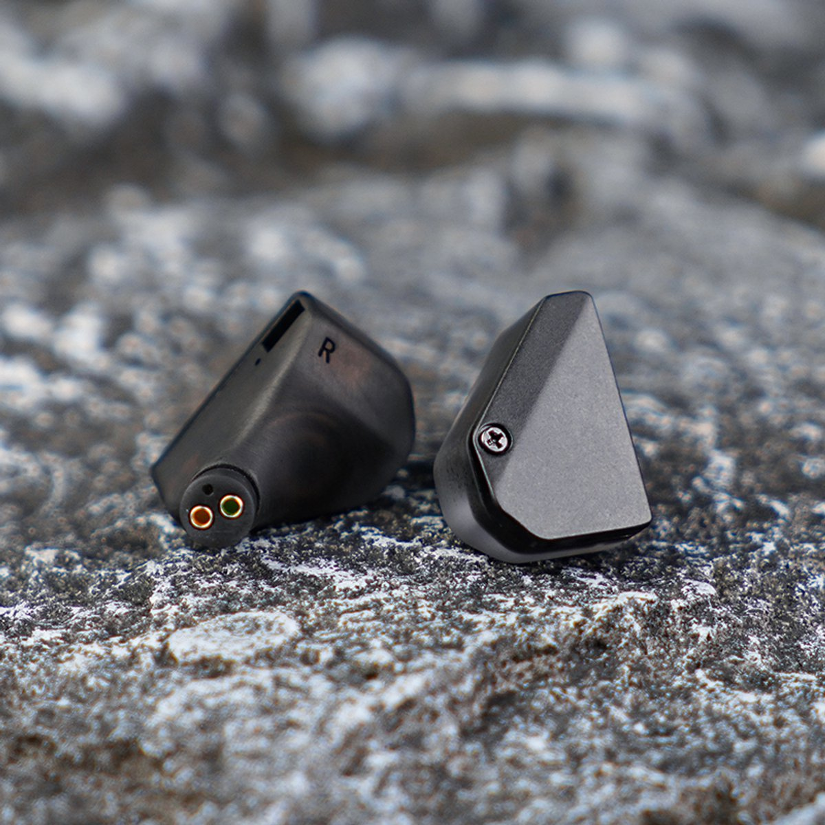 Zwei schwarze In-Ear-Kopfhörer auf einer strukturierten grauen Oberfläche. Einer zeigt 'R'. Nahaufnahme auf Details.