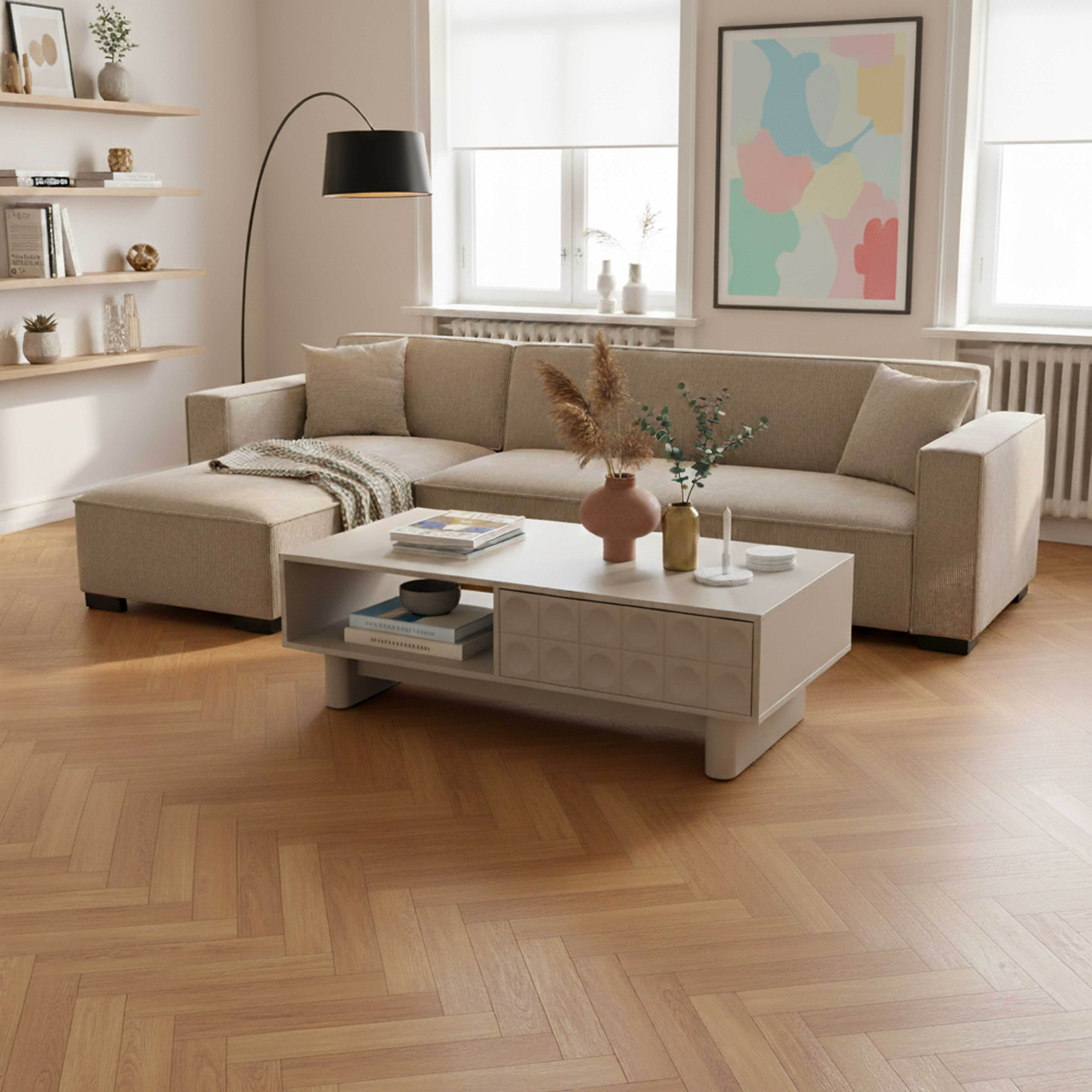 Beiges Ecksofa, Couchtisch mit Deko und Gemälde. Holzboden, Fenster und eine Stehlampe.