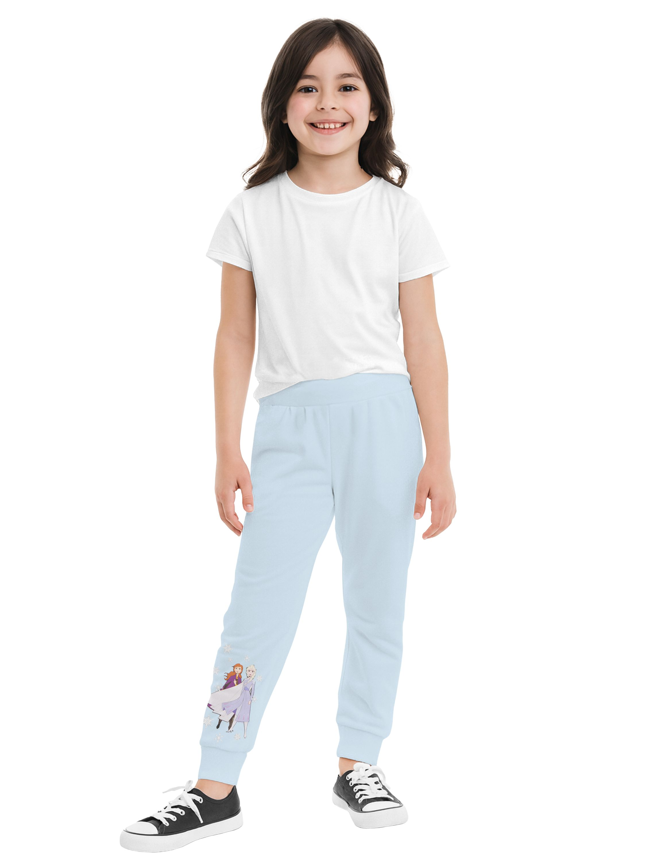 Ein Mädchen in weißem T-Shirt und hellblauer Hose mit Zeichentrickfiguren. Sie trägt Turnschuhe und lächelt in die Kamera.