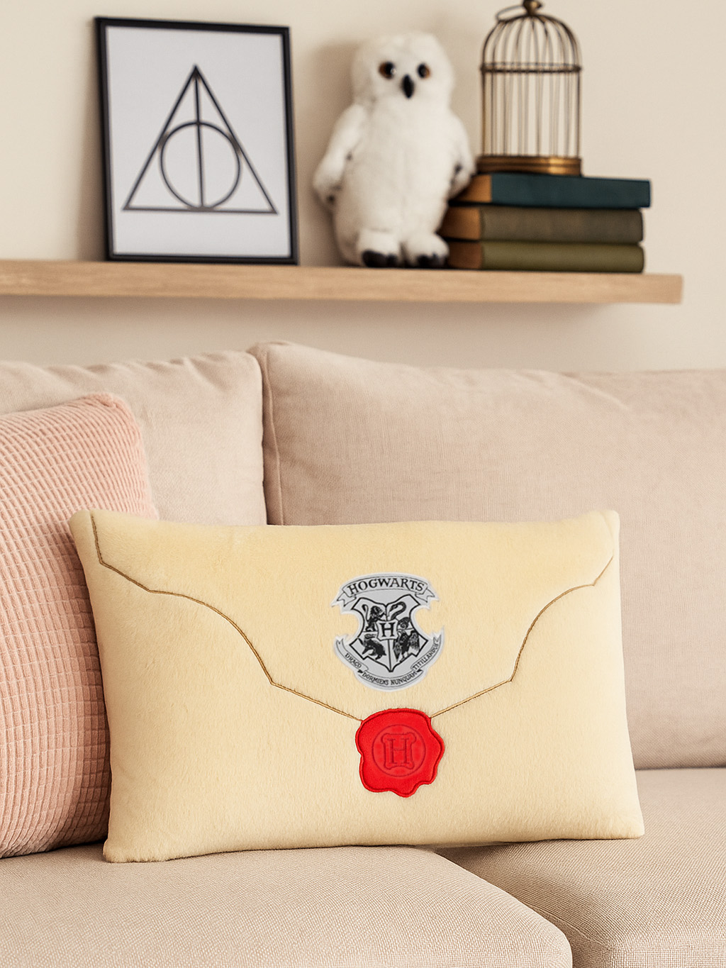 Ein cremefarbenes Kissen mit Hogwarts-Wappen, rotem Siegel und Goldstich auf einer beigen Couch.