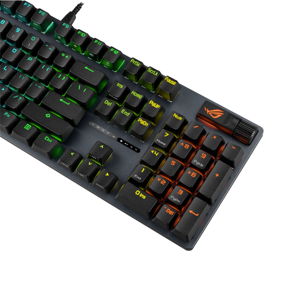 Un primo piano di una tastiera ROG nera con tasti illuminati in verde e arancione. La tastiera è su una superficie bianca.