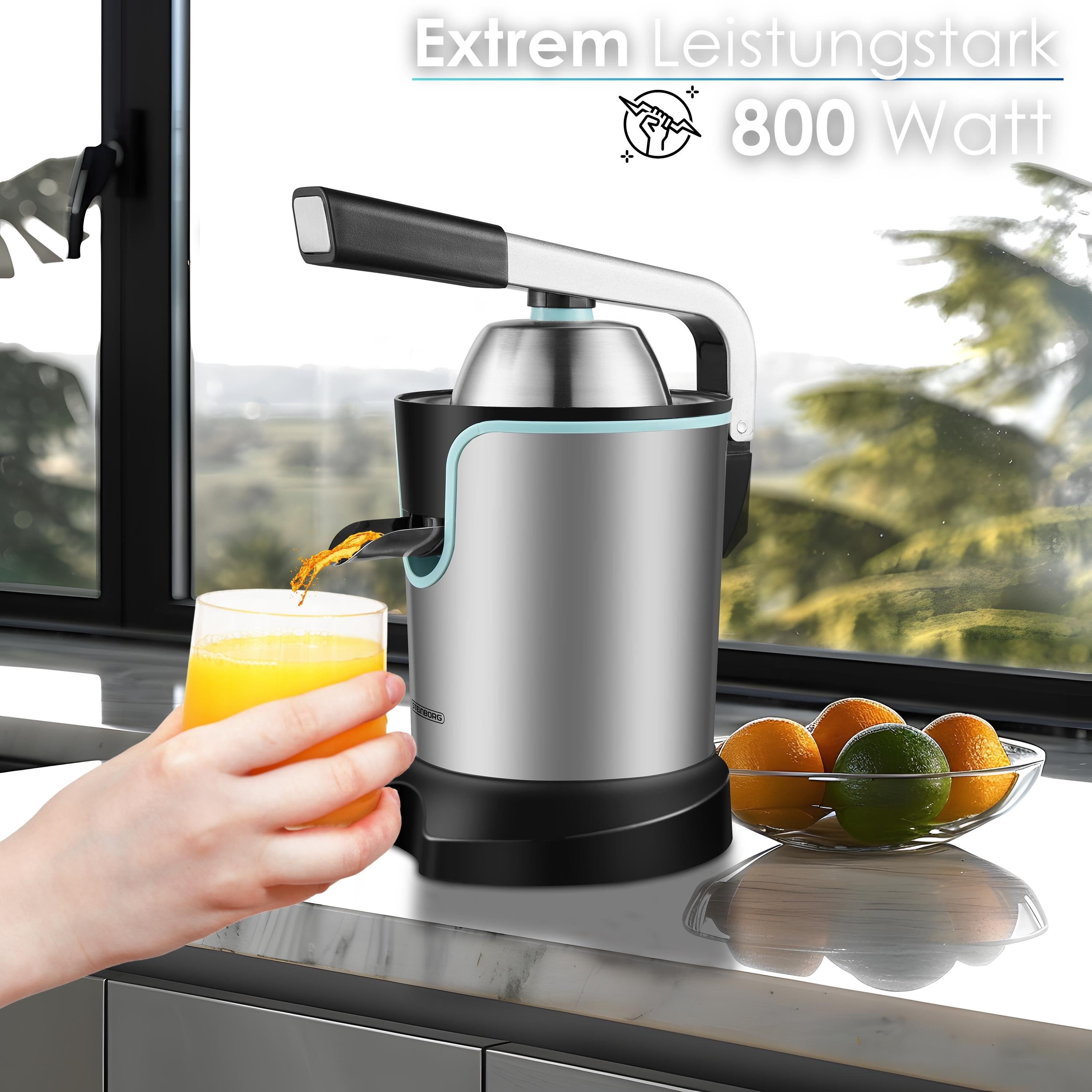 Ein Entsafter gießt Orangensaft in ein Glas. Orangen und Limetten befinden sich in einer Glasschüssel.