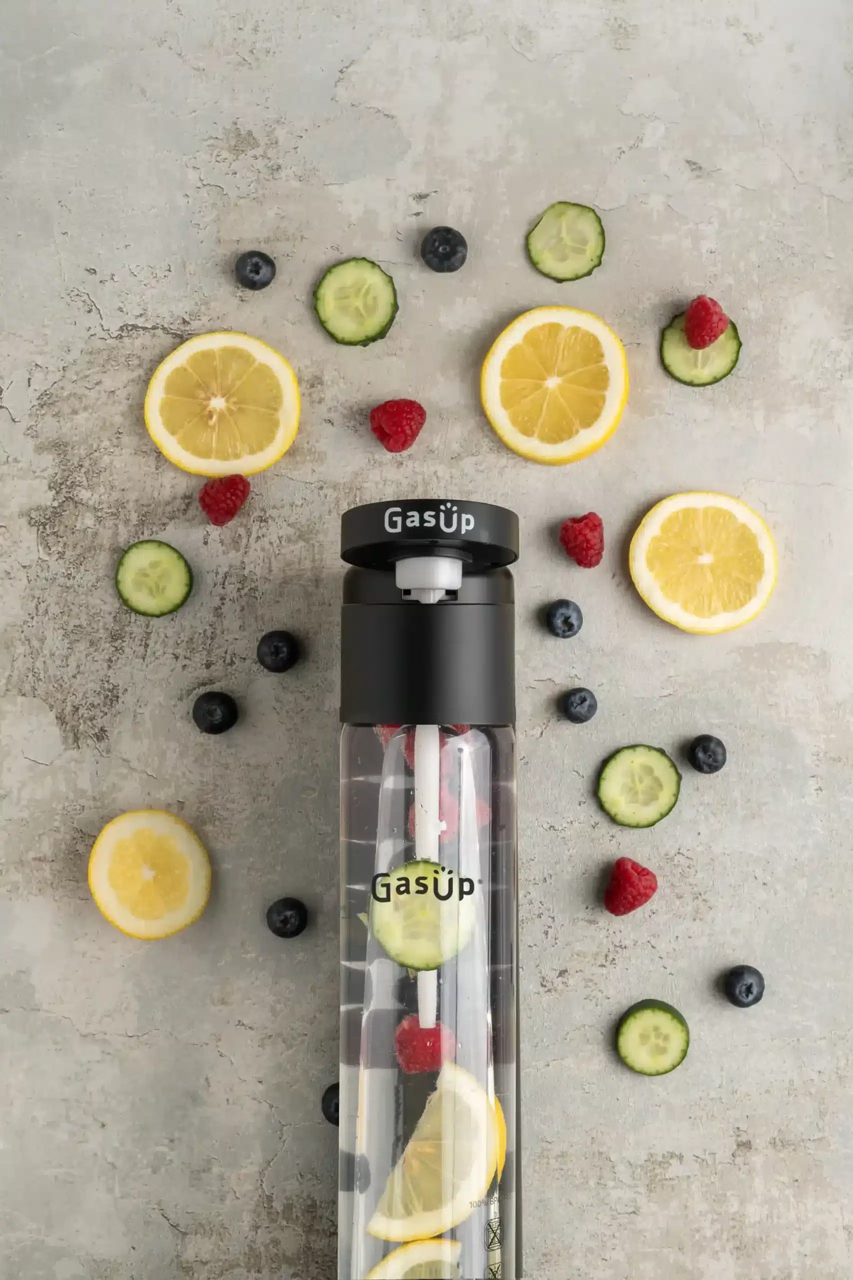 Una bottiglia d'acqua trasparente con frutta all'interno, circondata da fette di limone, mirtilli, lamponi e cetrioli.