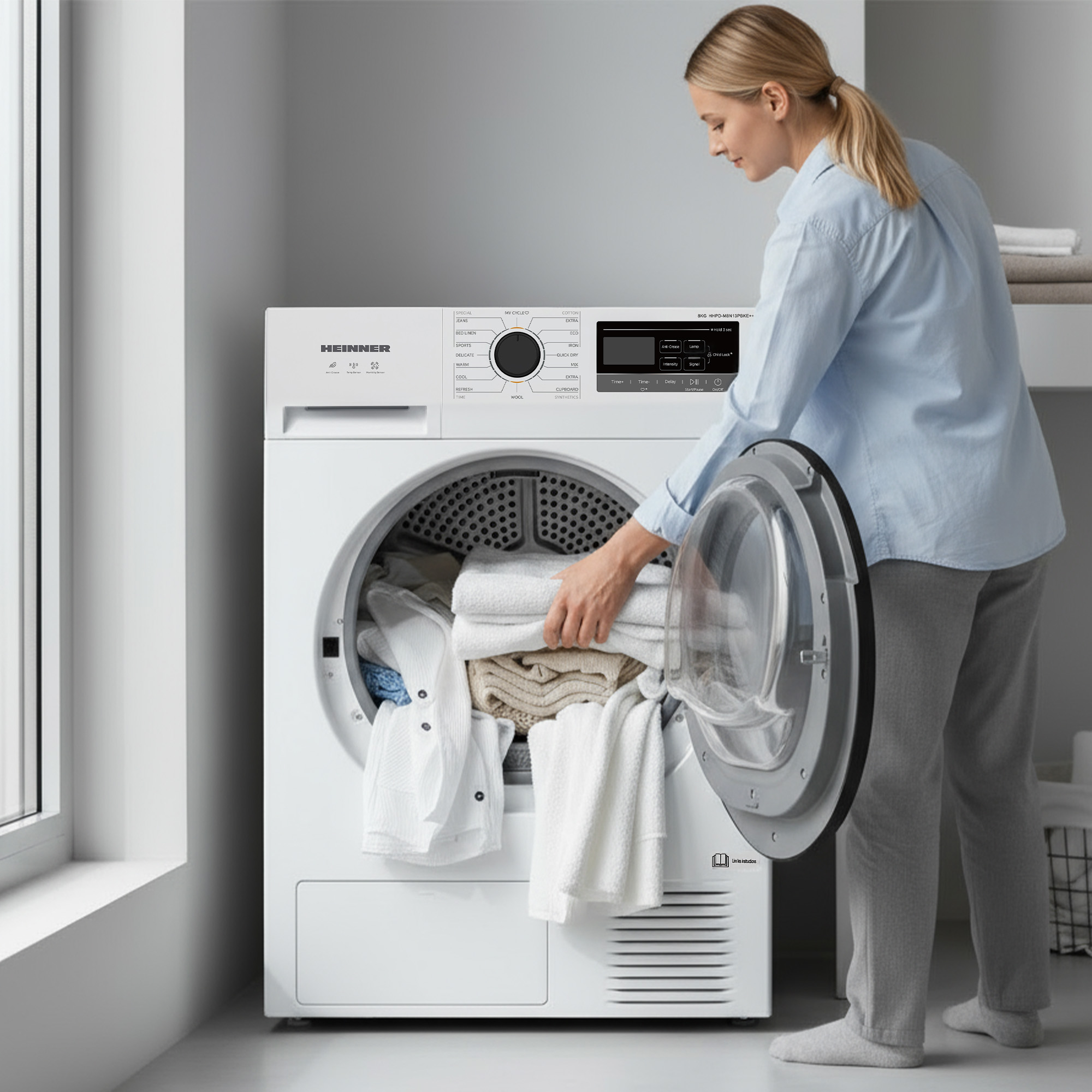 Een vrouw laadt een witte droger met kleding. De machine staat in een kamer met een raam.