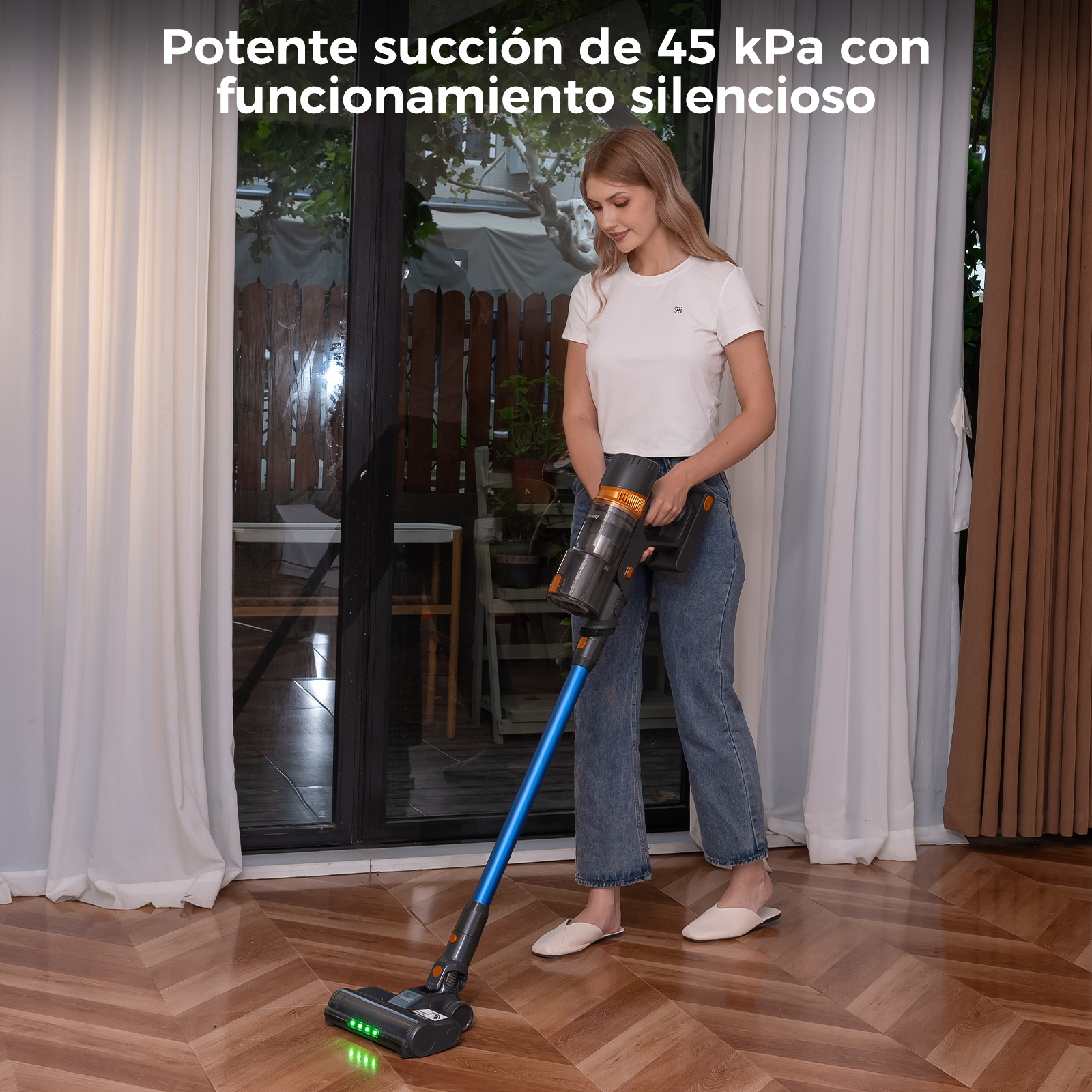 Una mujer usa una aspiradora inalámbrica en un piso de madera. Usa jeans y una camisa blanca.