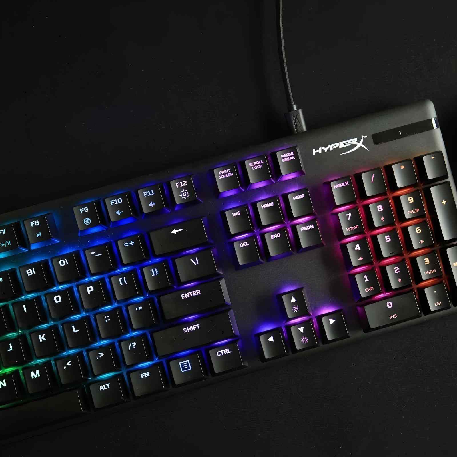Un primo piano di una tastiera HyperX nera. I tasti sono illuminati da luci colorate. Un cavo è collegato.