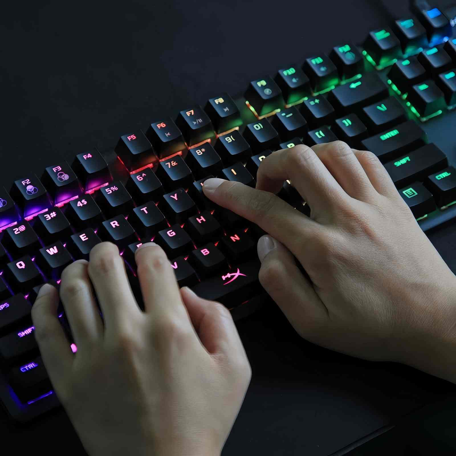 Mani che digitano su una tastiera retroilluminata. I tasti sono neri con illuminazione a LED colorata. La scena è scura.