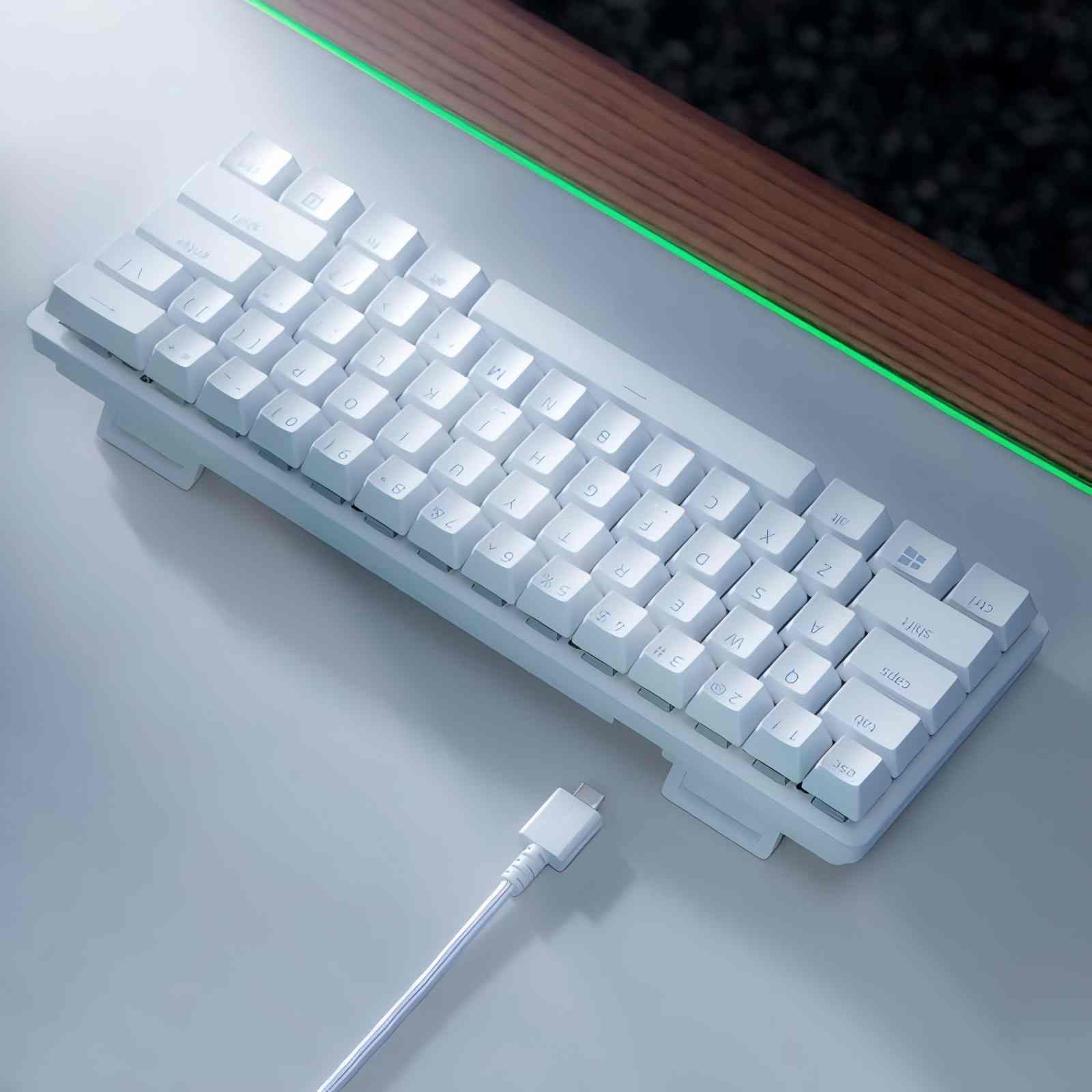 Tastiera bianca con tasti bianchi e cavo USB-C. Lo sfondo è grigio e un bordo in legno.