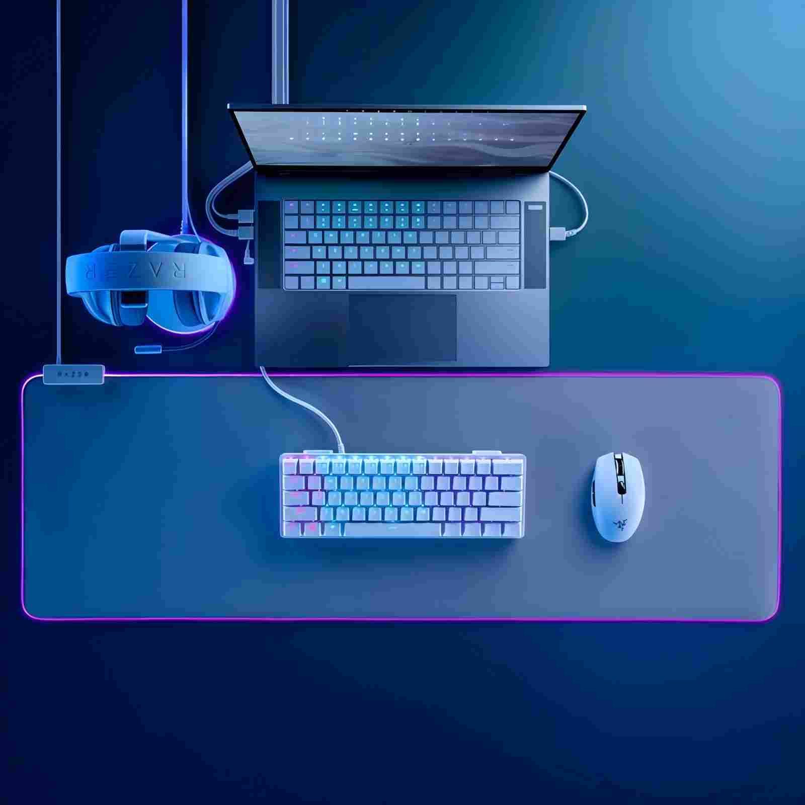 Un setup da gaming con laptop, tastiera, mouse e cuffie. Tutto illuminato di blu su una superficie blu-viola, Razer.
