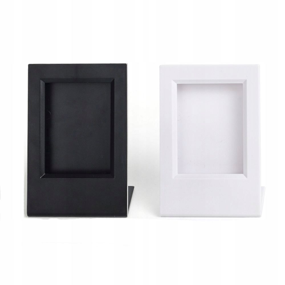 Dwie ramki na zdjęcia, jedna czarna i jedna biała, stoją obok siebie na białej powierzchni. Mają prostokątny kształt.