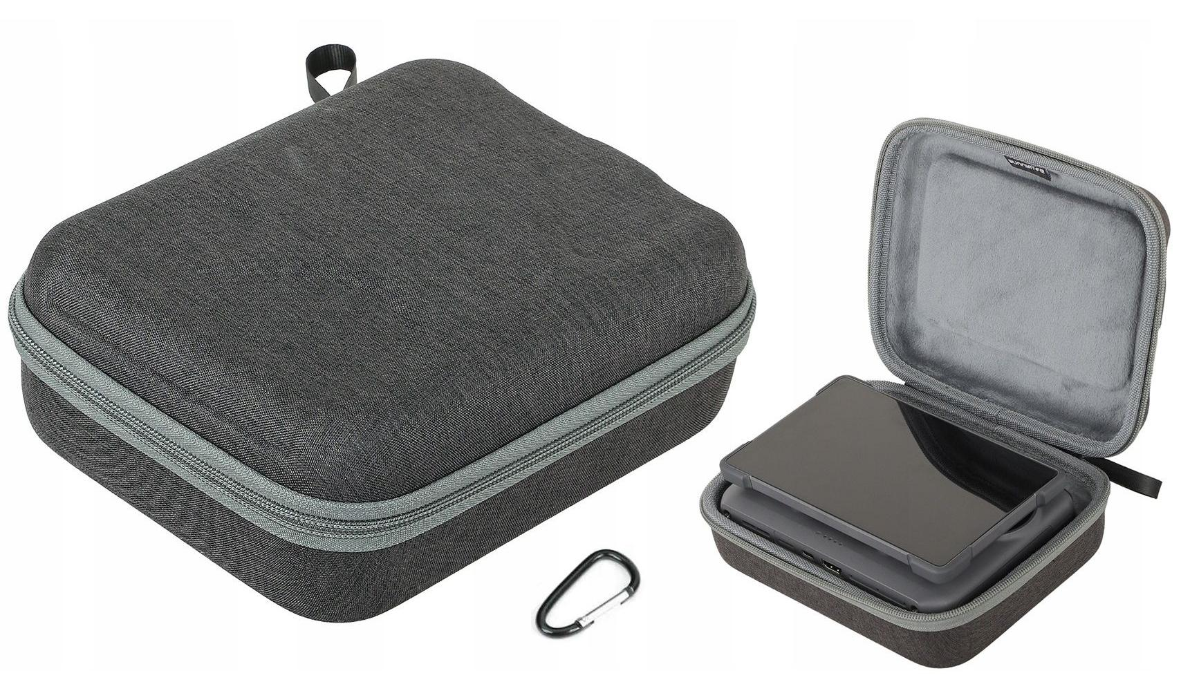 Szara zapinana na zamek torba, otwarta torba z urządzeniem w środku. Karabińczyk jest na dole pośrodku.