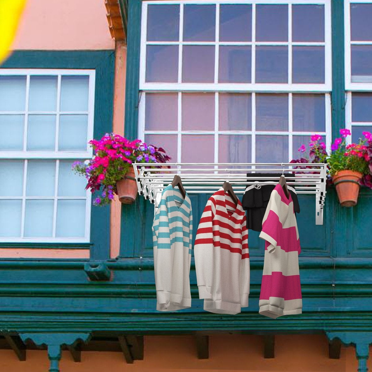Ropa colgada en un tendedero. Camisas a rayas y una camisa negra cuelgan frente a una ventana y flores.