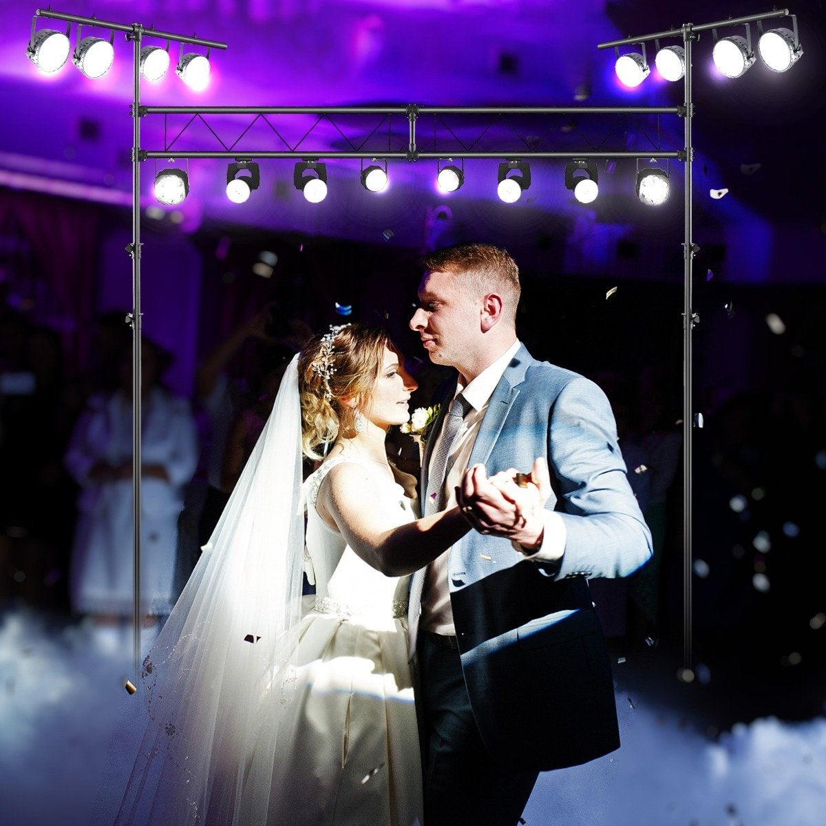 Una novia y un novio bailan en su boda. Las luces del escenario los iluminan. Cae confeti. La gente está borrosa en el fondo.