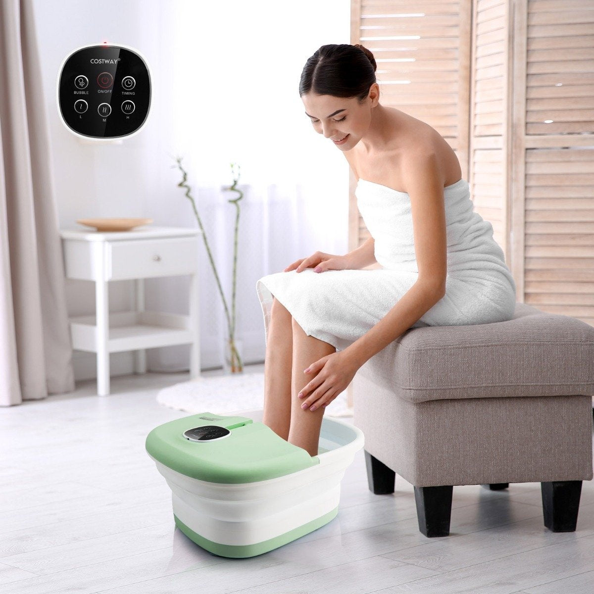 Una mujer con una toalla blanca se sienta, metiendo los pies en un baño de pies. Un ambiente de spa. Un panel de control en la pared.
