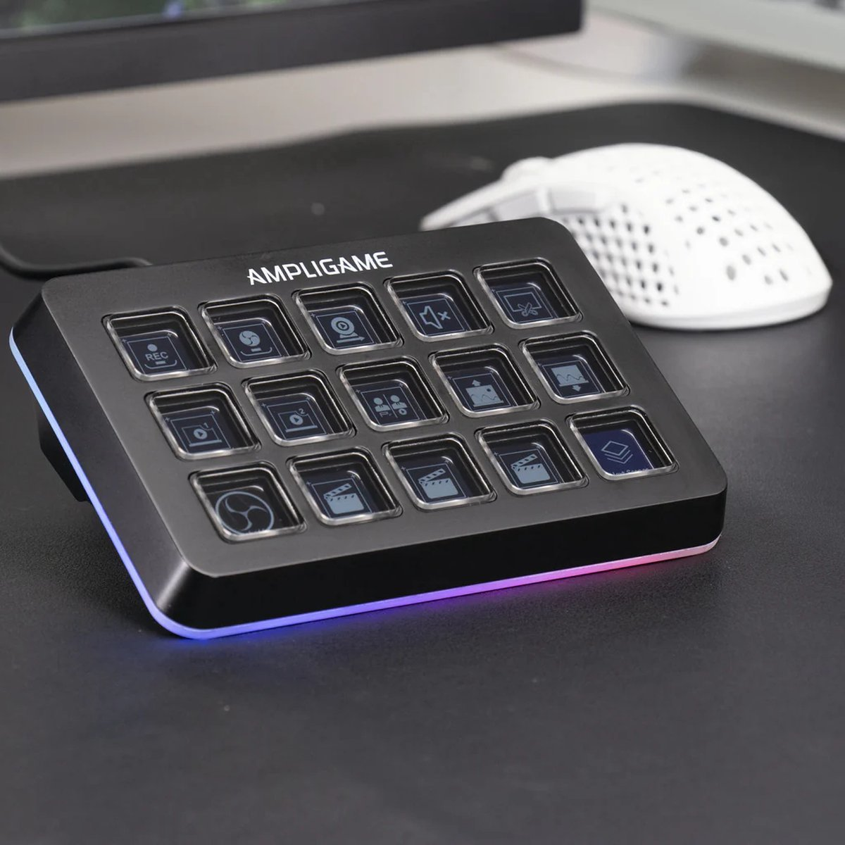 Black Ampligame control panel with 15 buttons, icons on them, and a white mouse on a black desk. The panel has a colorful edge.