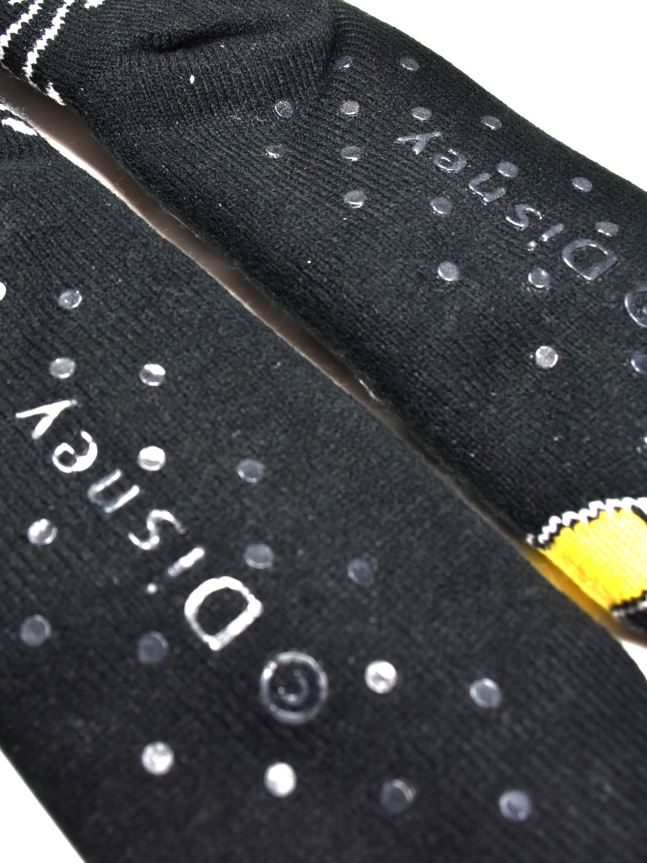 Nahaufnahme von schwarzen Disney-Socken mit weißer Schrift und Greifpunkten. Weiße und gelbe Akzente sind sichtbar.