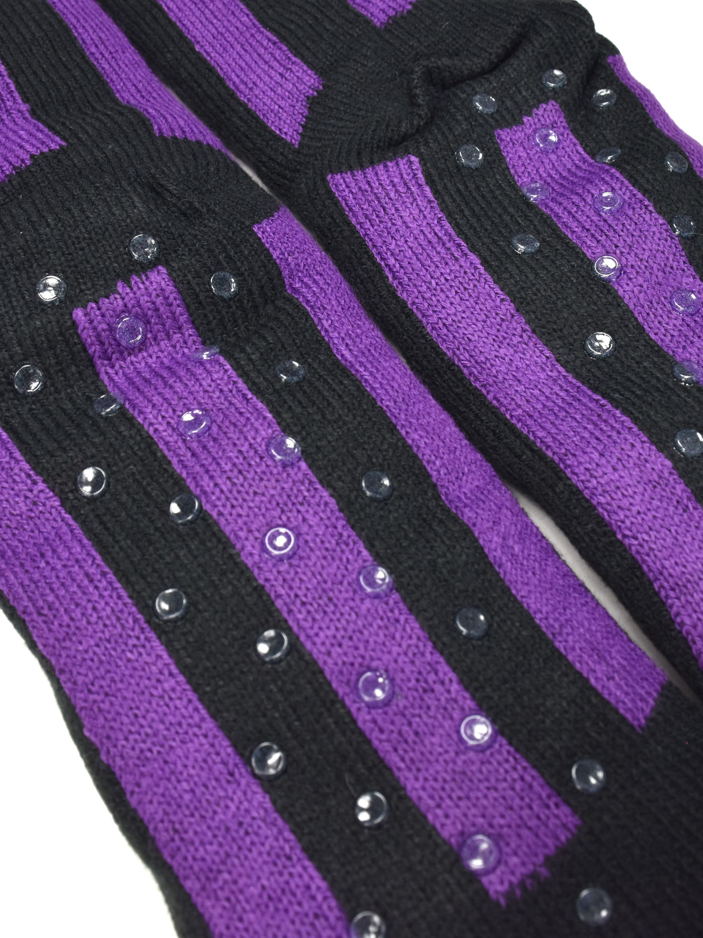 Paar Socken mit lila und schwarzen Streifen. Klare, runde Griffe befinden sich auf den Sohlen.