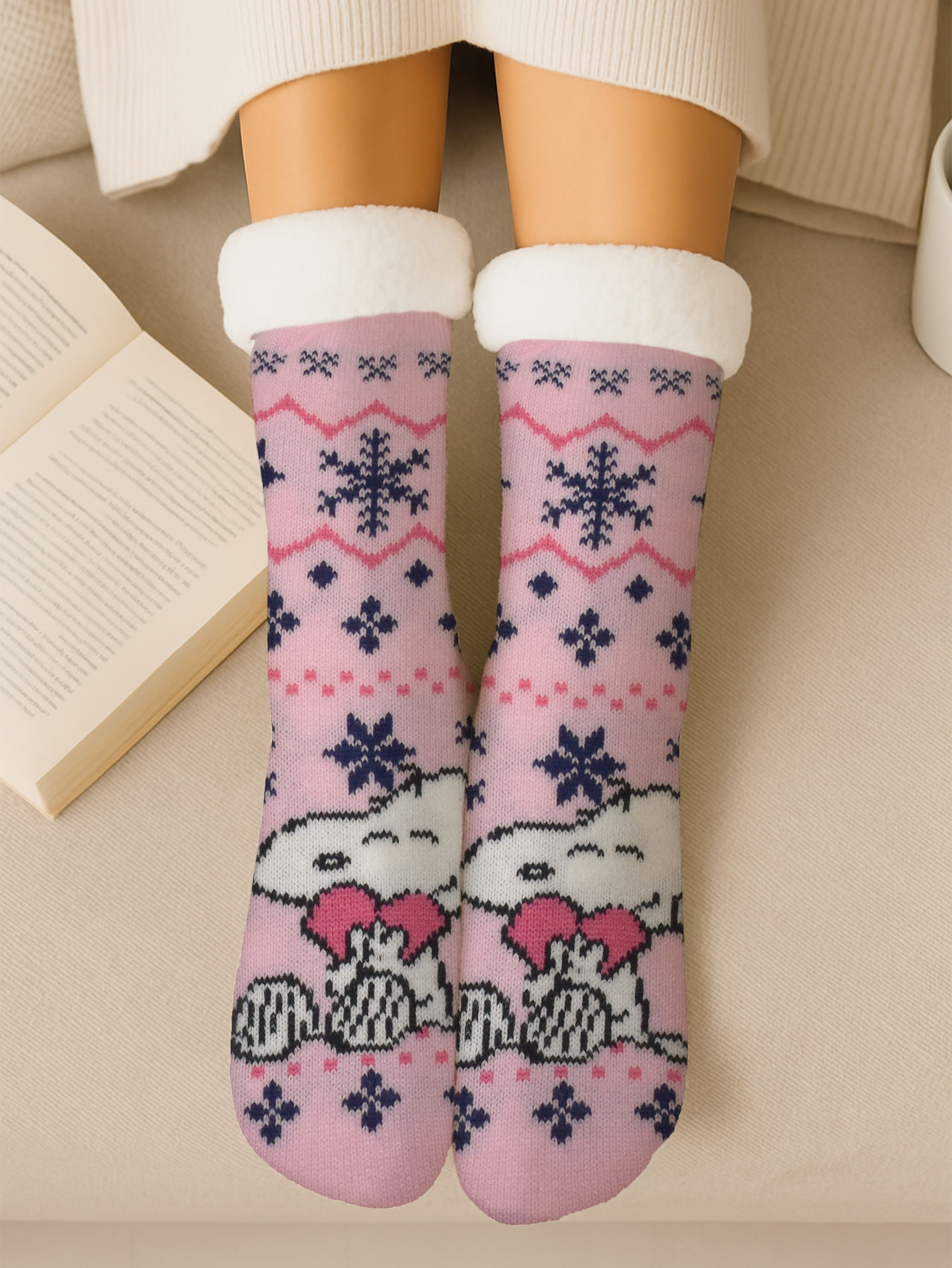Rosa Socken mit Snoopy-Design, weißem Besatz und einem Buch. Beine sind sichtbar, ruhen auf beiger Oberfläche.