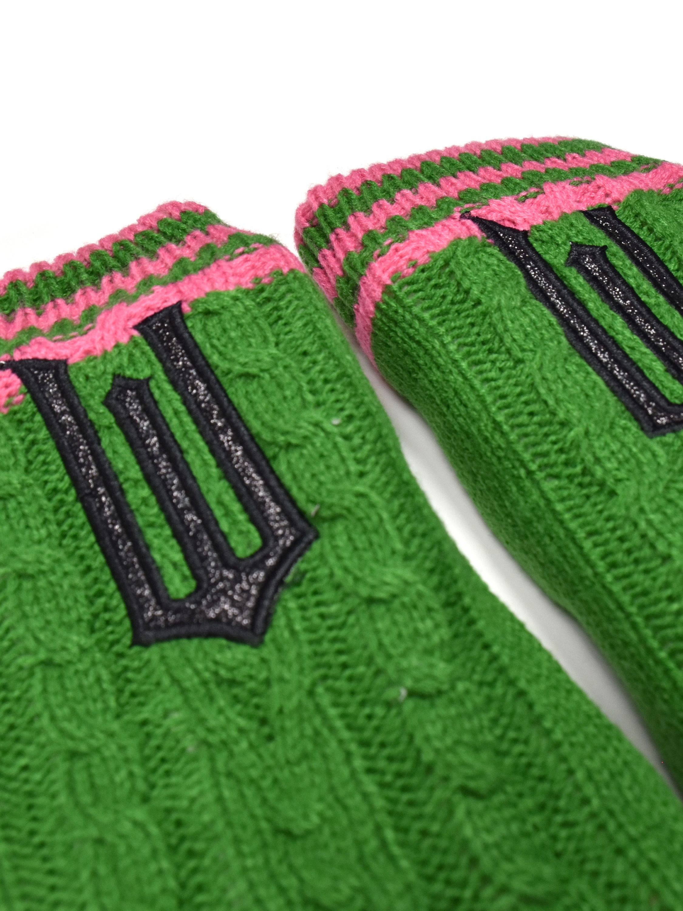 Zwei grüne Stricksocken mit rosa Streifen oben und schwarzen Dreizack-Symbolen.