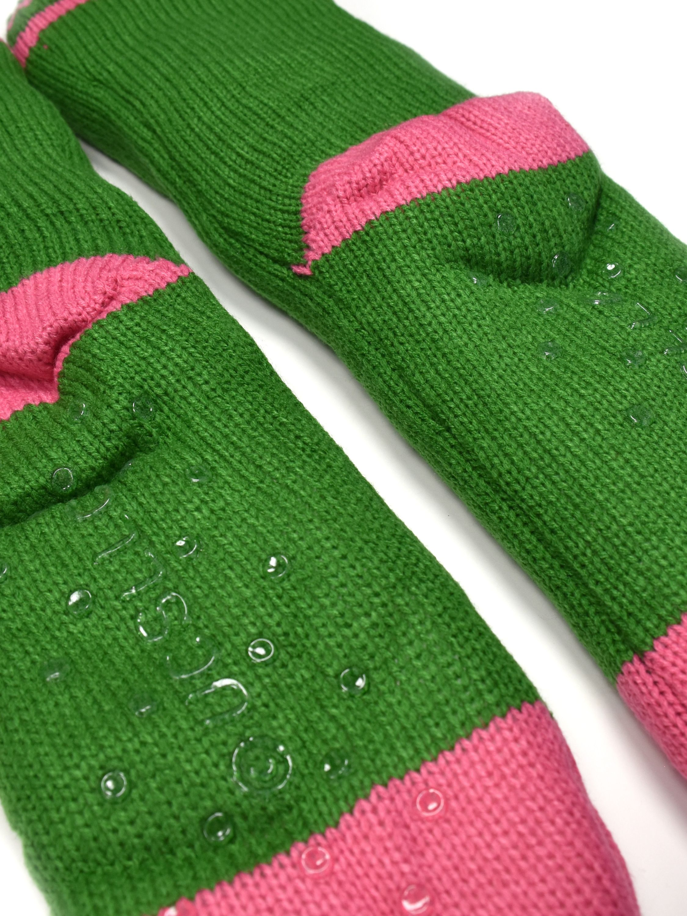 Grüne gestrickte Socken mit pinkfarbenen Bündchen. Klare Anti-Rutsch-Griffe befinden sich auf den Sohlen. Weißer Hintergrund.