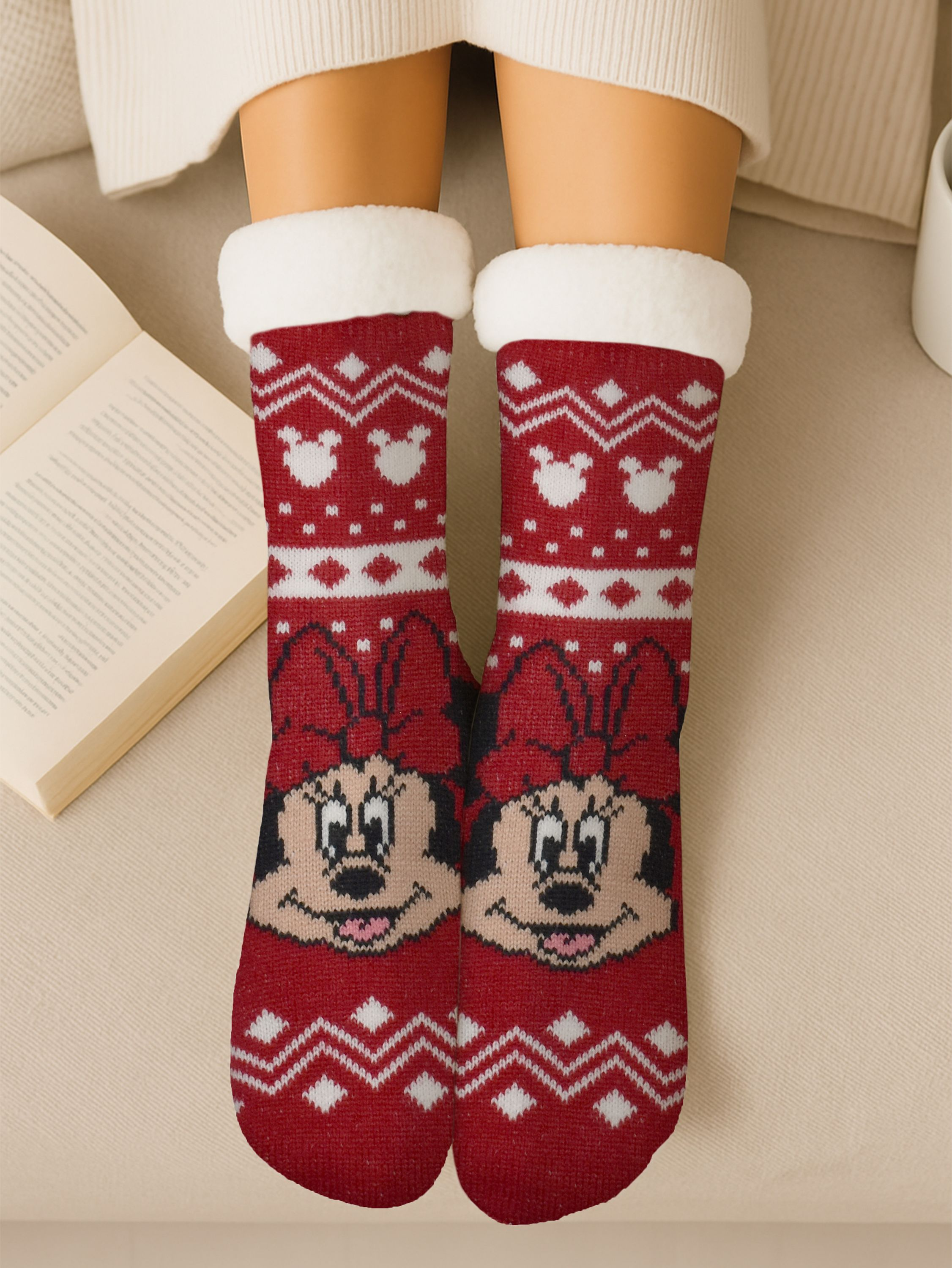 Rote Minnie-Maus-Socken mit weißem Besatz und Design. Offenes Buch links, Beine und Pullover sichtbar.