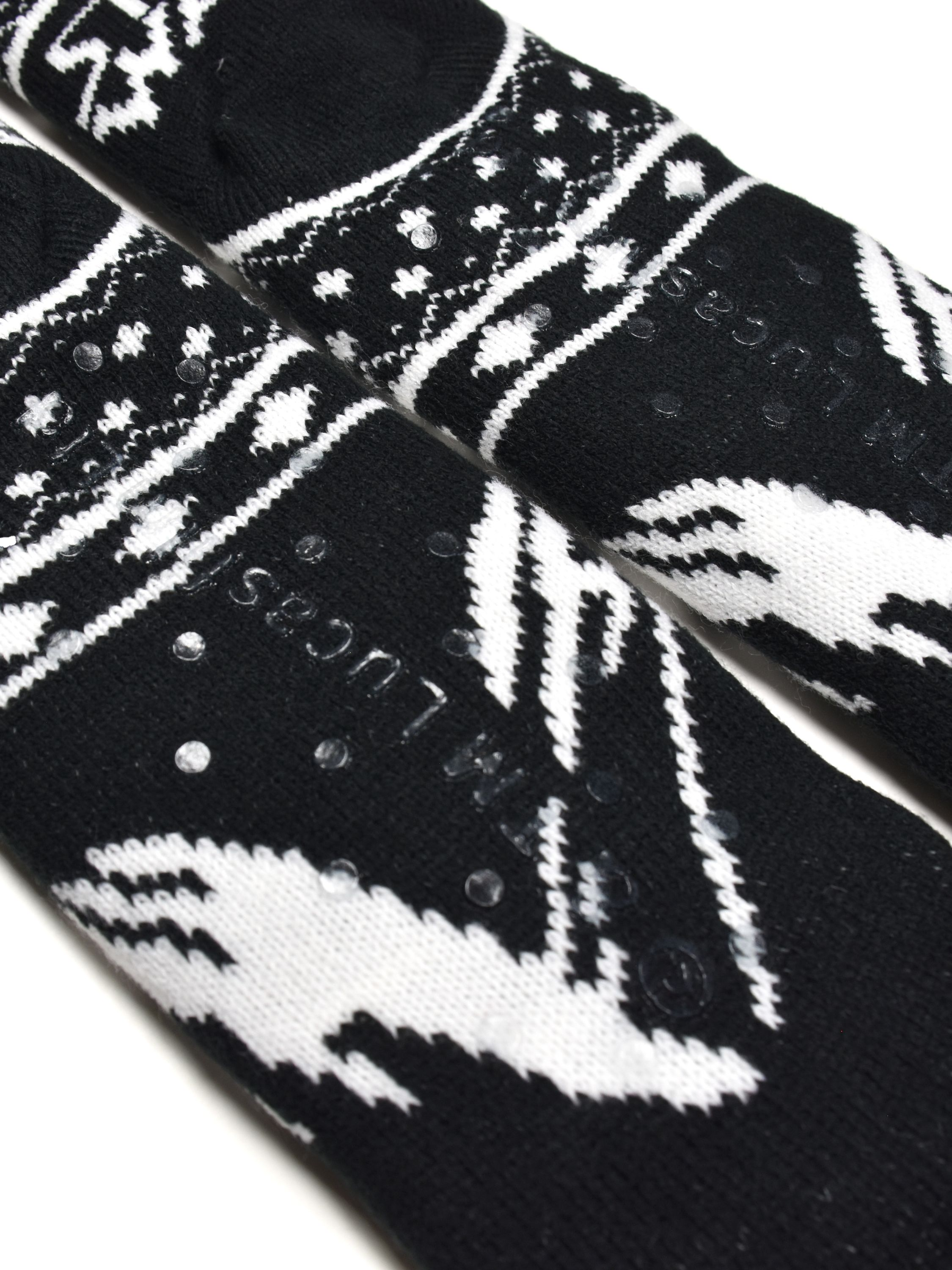 Zwei schwarz-weiß gemusterte Socken. Sie haben weiße Muster und kleine, durchsichtige Grip-Punkte. Die Marke TM Lucas ist sichtbar.