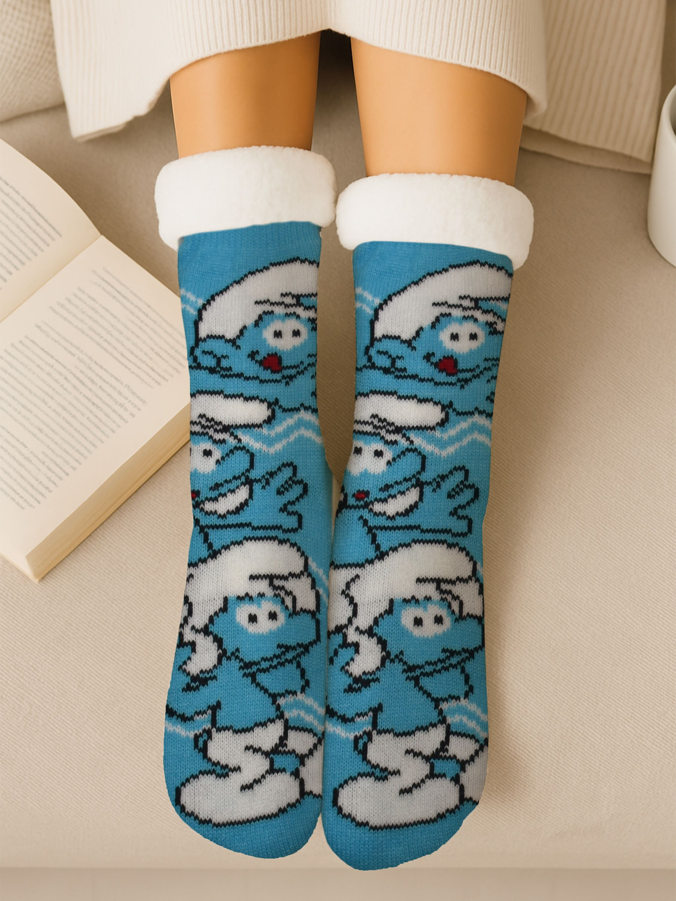 Person trägt blaue Schlumpfsocken mit weißer Bordüre und sitzt auf beiger Oberfläche mit einem Buch.