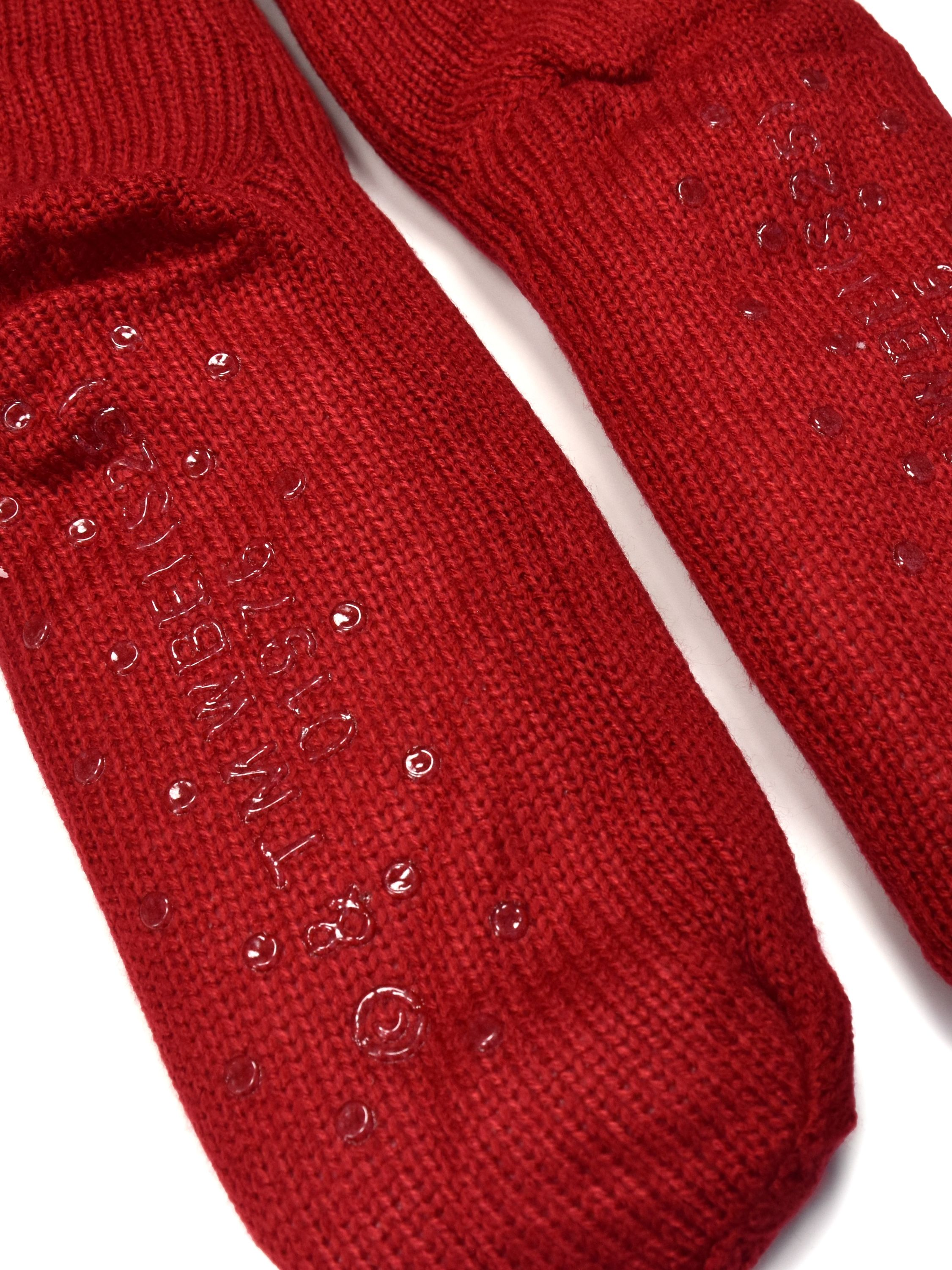 Zwei rote Socken mit durchsichtigen, kreisförmigen Griffen sind abgebildet. Weißer Hintergrund. Die Socken haben Text und Punkte auf der Unterseite.