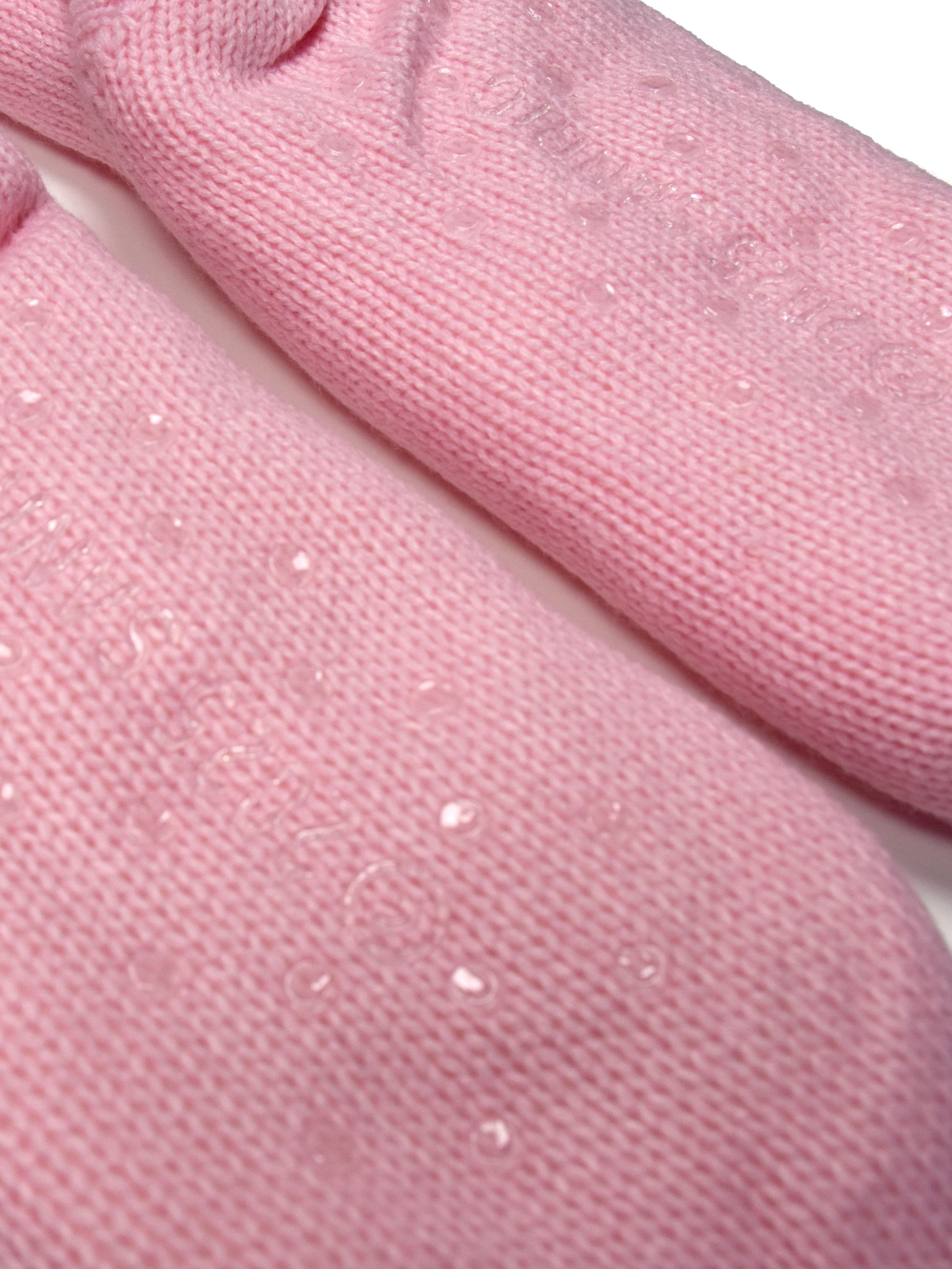 Nahaufnahme von rosa Strickstoff mit Wassertropfen. Der Stoff ist leicht strukturiert, die Tropfen klar.
