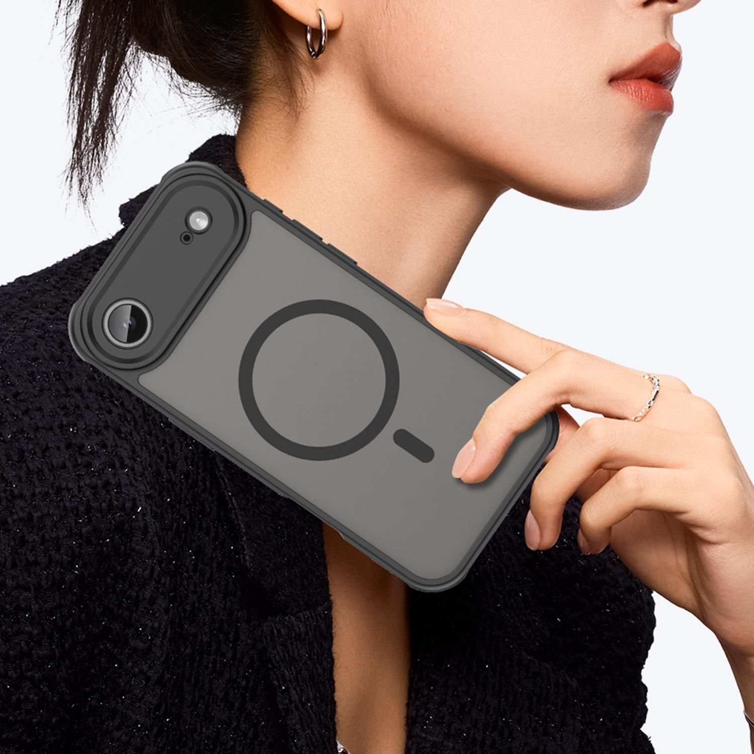 Una persona sostiene una funda de teléfono gris con un recorte para la cámara. La persona lleva una chaqueta negra, un anillo y un pendiente de aro.
