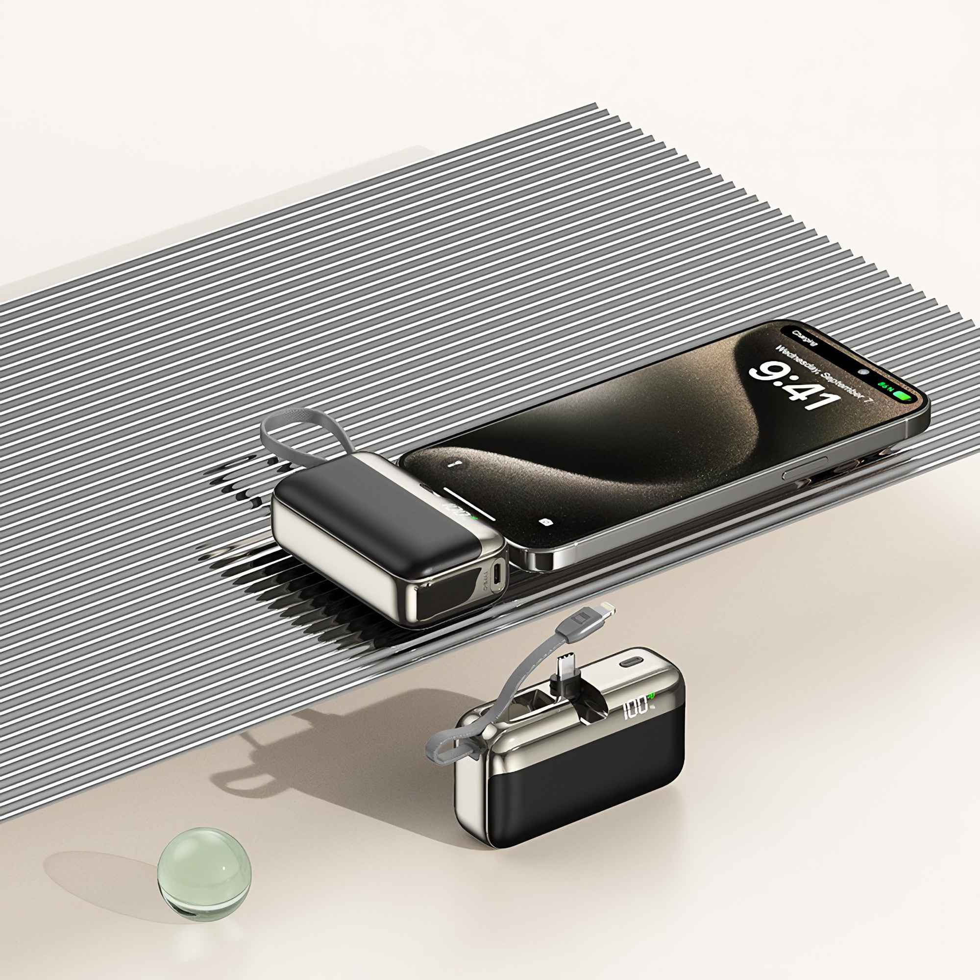 Ein Telefon, das aufgeladen wird, ist mit zwei Powerbanks verbunden und liegt auf einer grau gestreiften Oberfläche. Eine Glaskugel liegt unten.