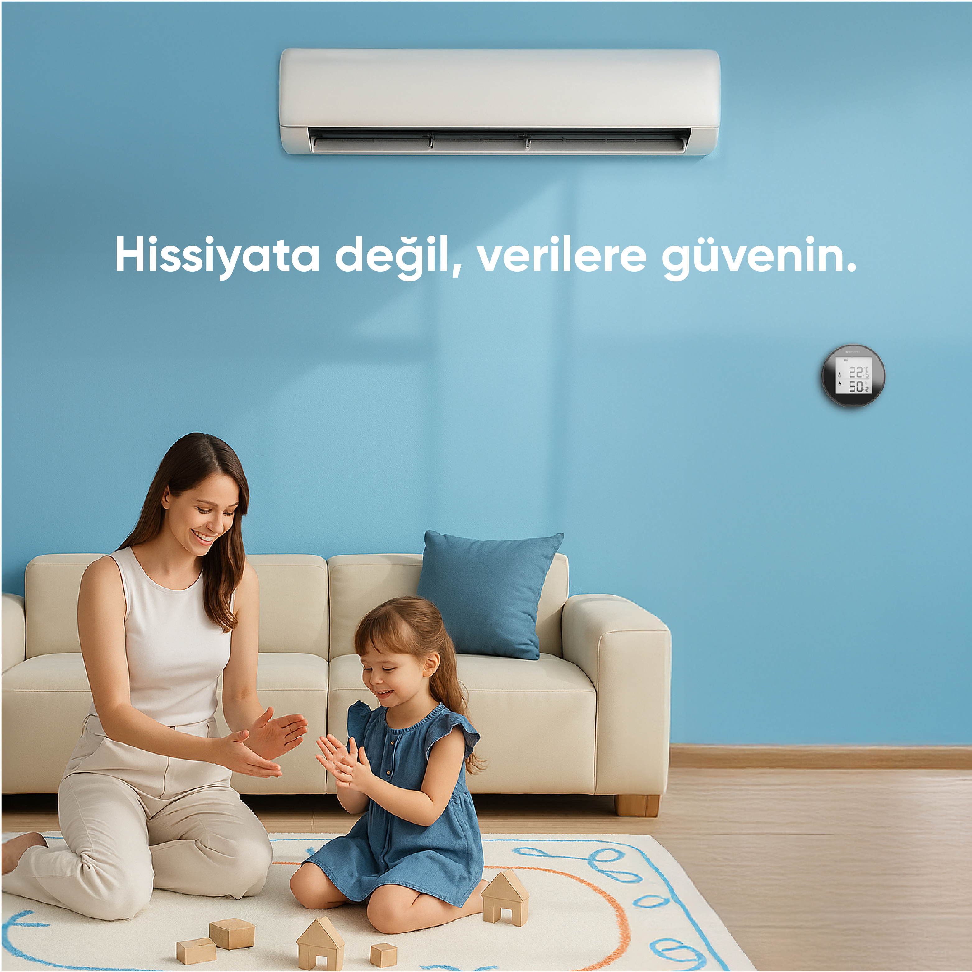 Bir kadın ve bir kız çocuk halıda tahta bloklarla oynuyor. Arkalarında bir kanepe ve mavi duvar var. Klima.