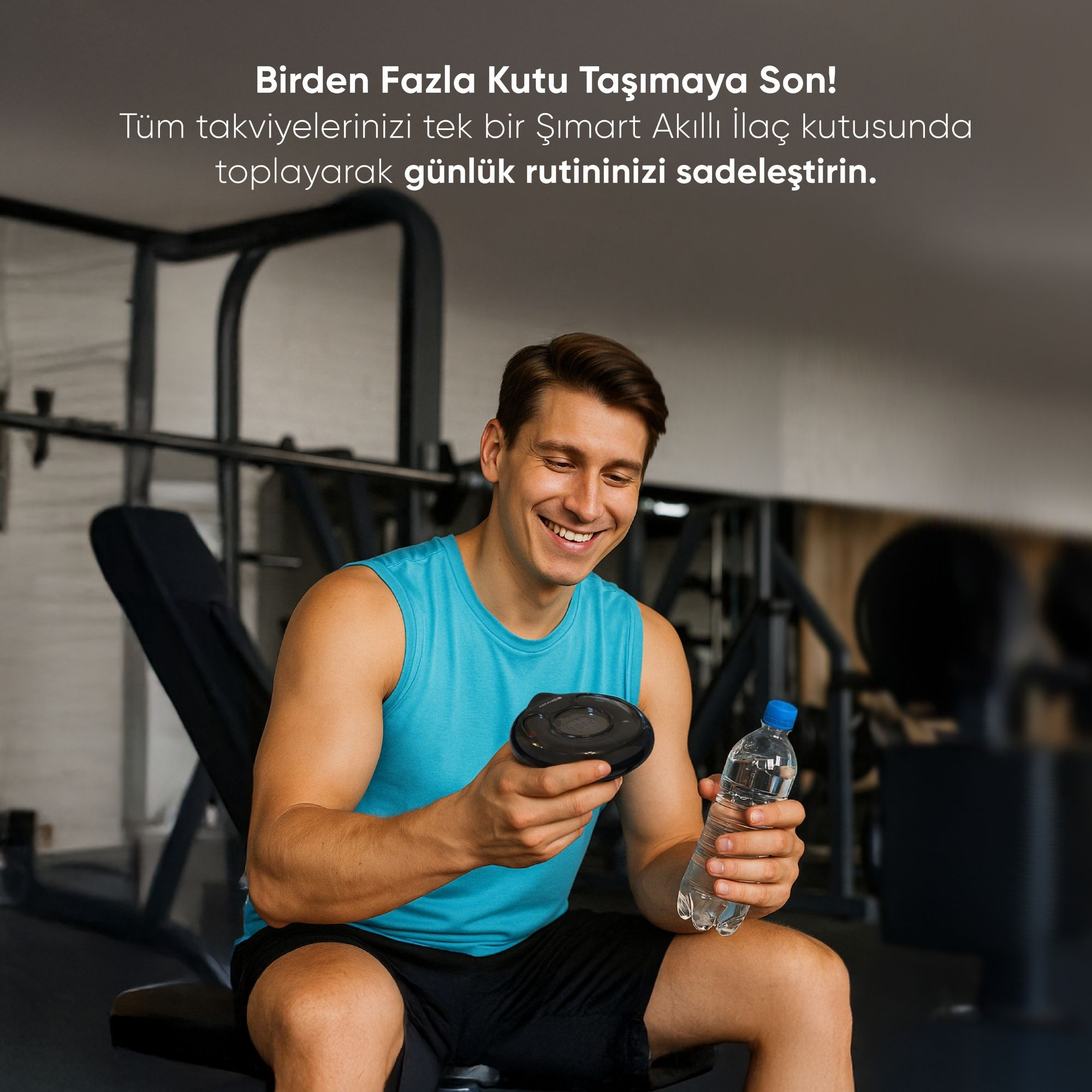 Spor salonunda siyah hap düzenleyici ve su şişesi tutan, gülümseyen adam. Arka planda spor ekipmanları.