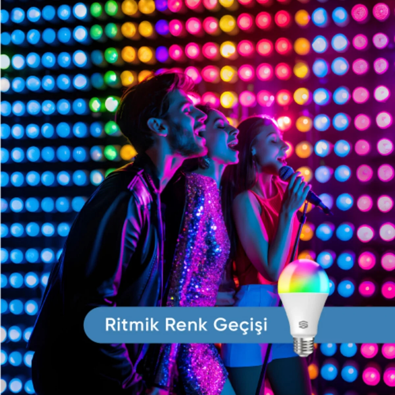 Üç kişi mikrofonlarla şarkı söylüyor. Renkli arka plan ışıkları. Renk geçişli bir ampul ön planda.