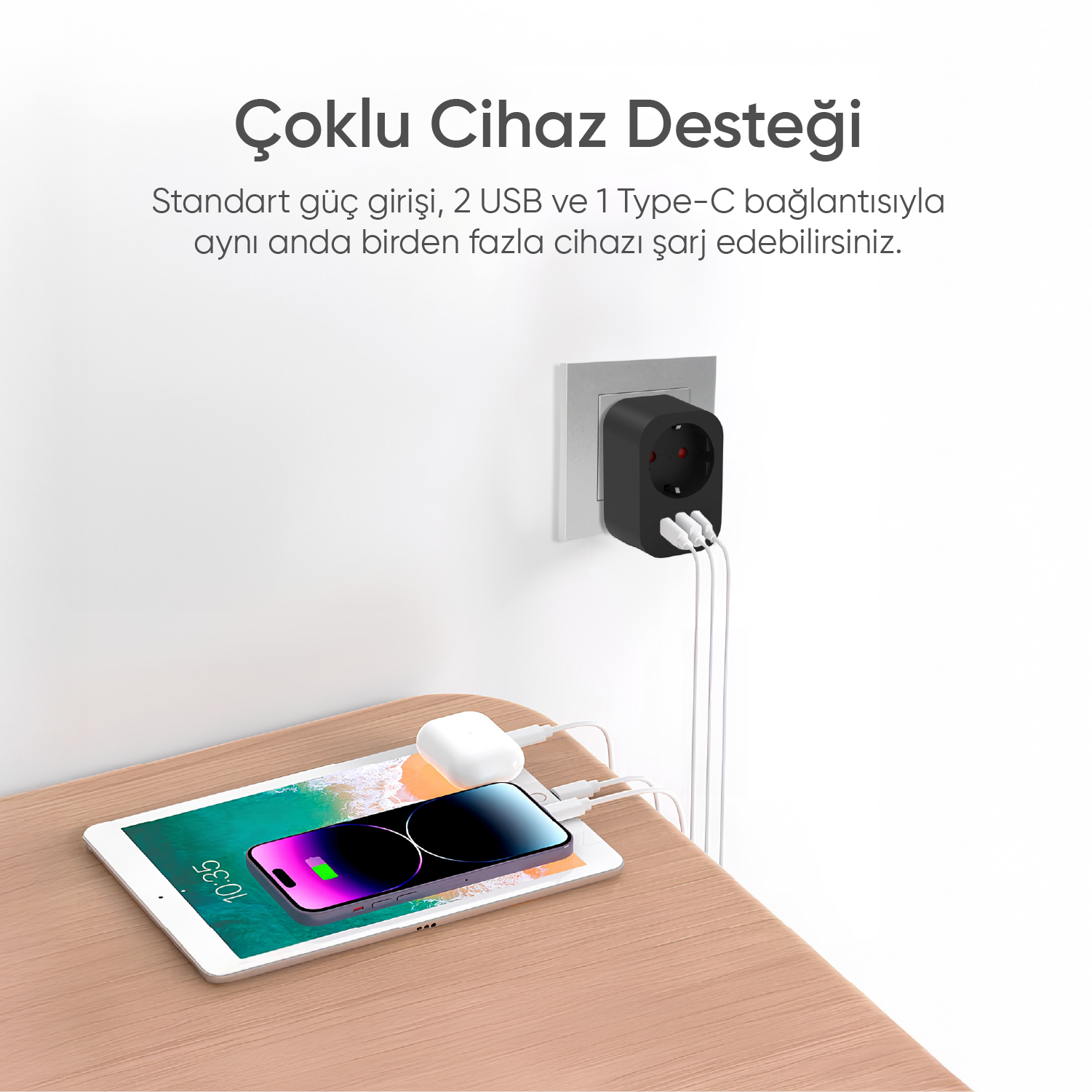 Çoklu USB portlu siyah bir güç adaptörü, ahşap bir masada bir tablet, telefon ve kulaklık şarj ediyor.