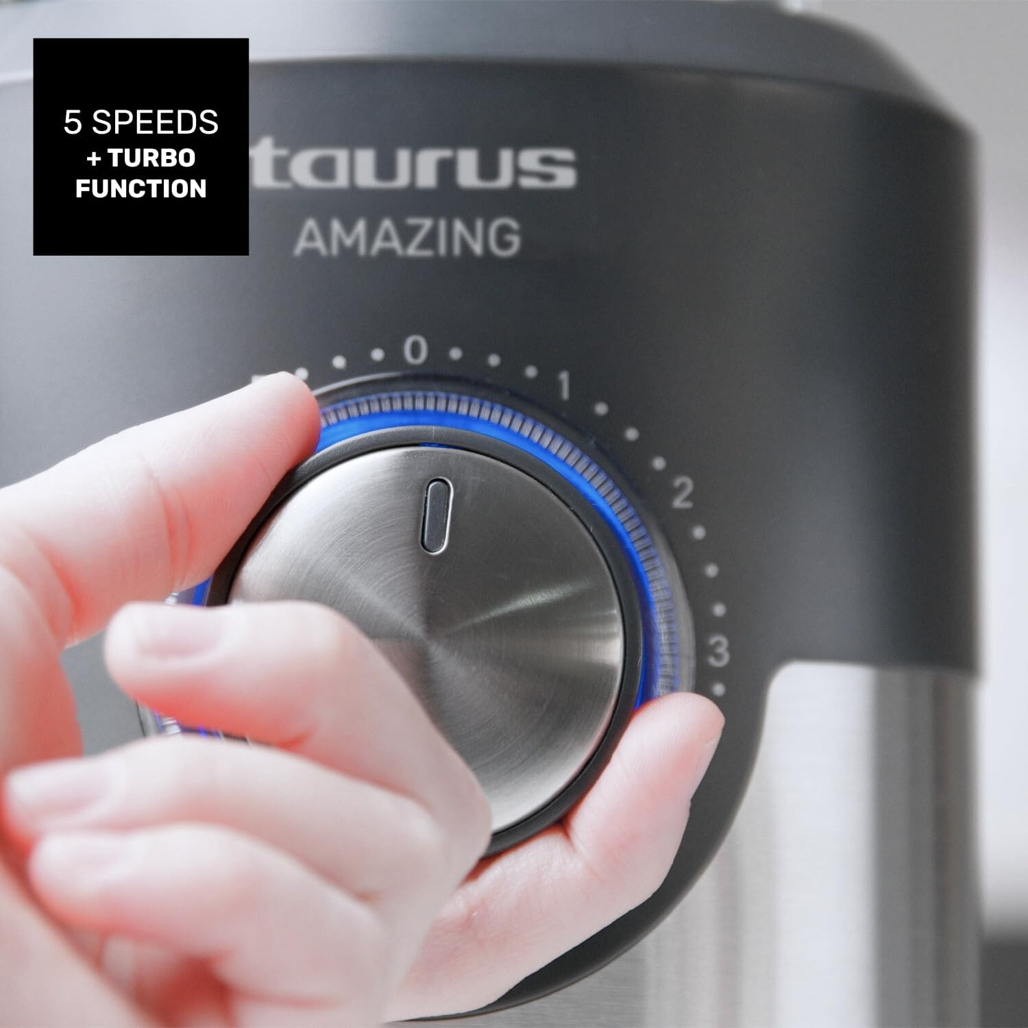 Una mano gira un dial en una batidora Taurus. El dial tiene una luz azul y números. El texto dice '5 velocidades + función Turbo'.