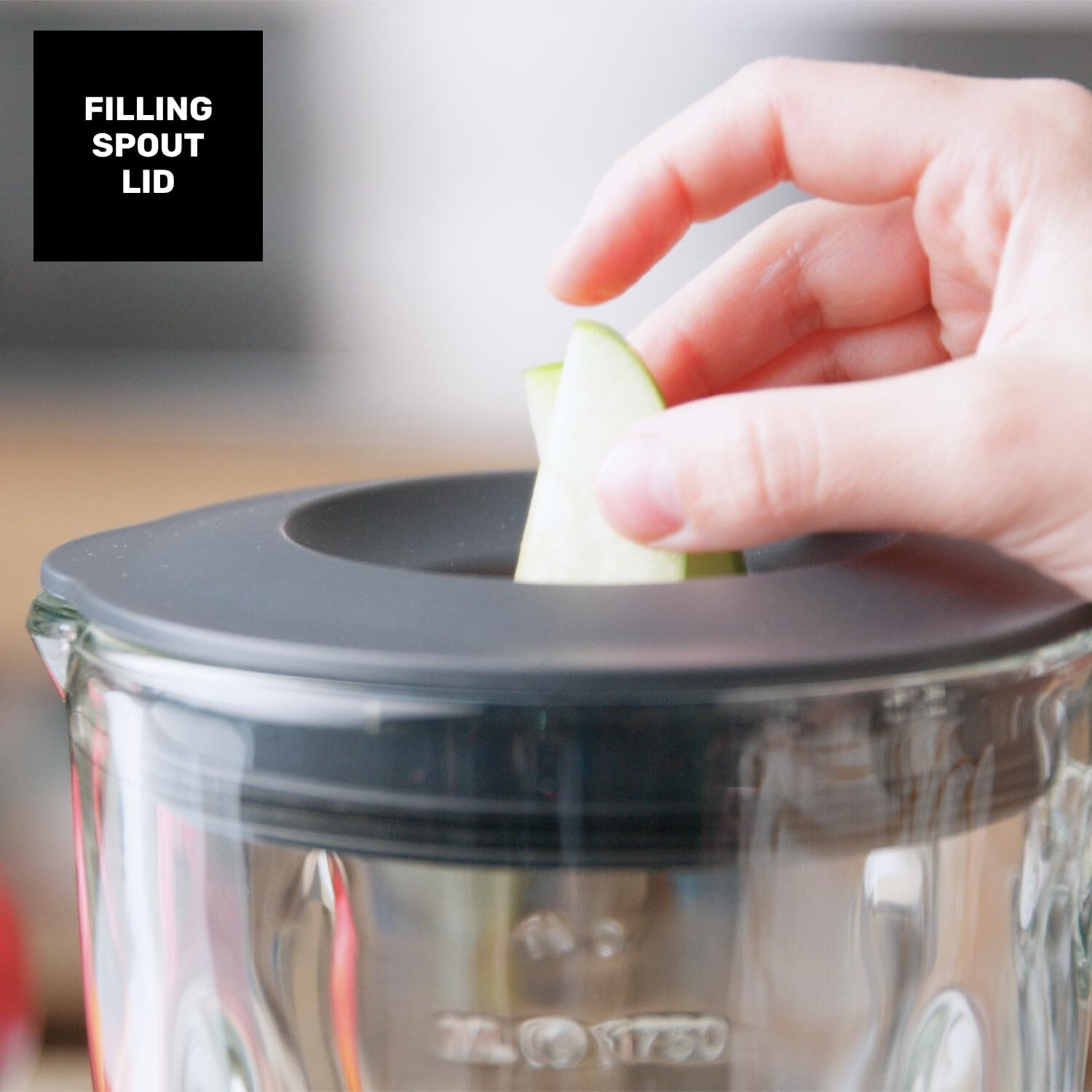 Una mano coloca una rodaja de manzana en un recipiente de vidrio. El recipiente tiene una tapa negra. Un letrero dice "FILLING SPOUT LID".
