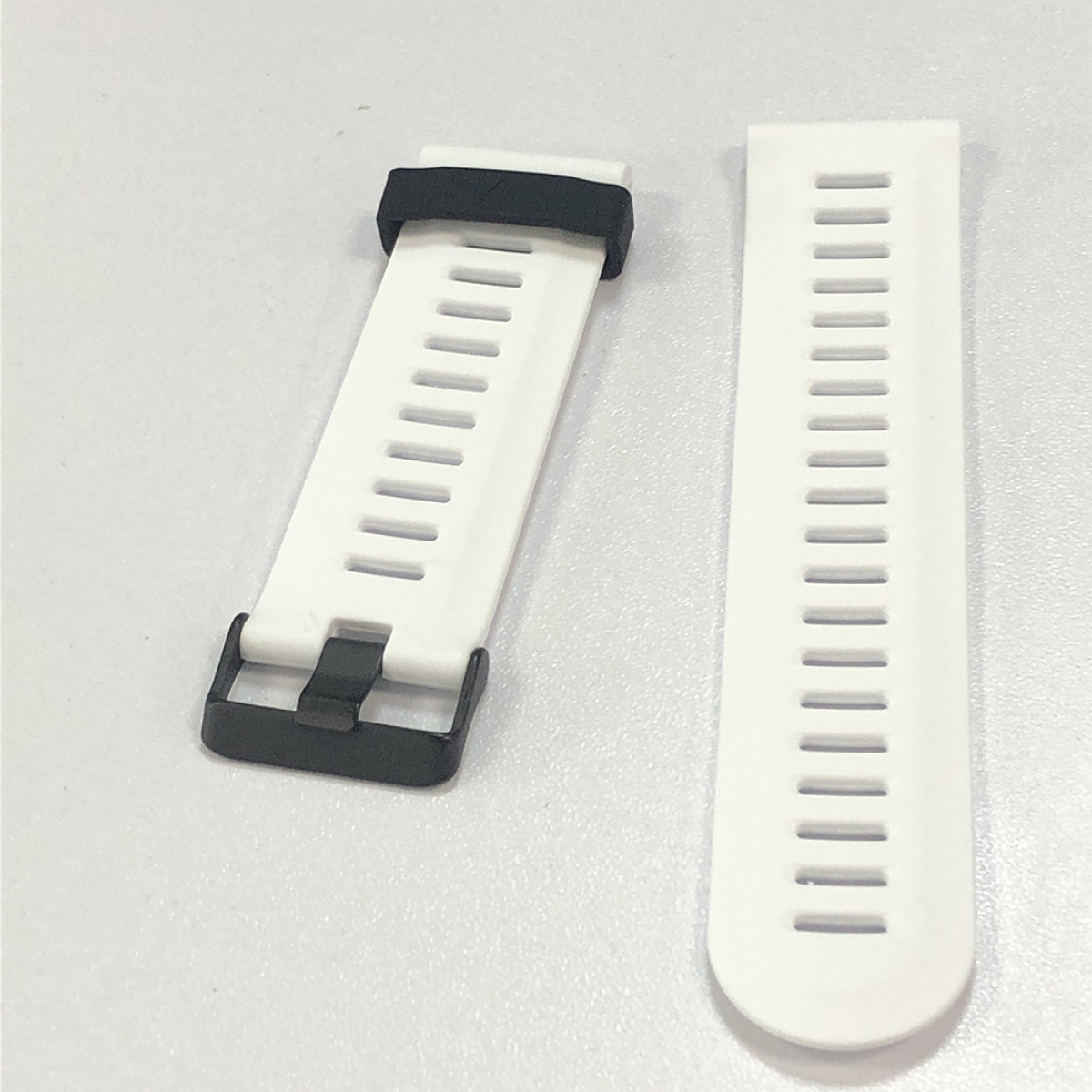 Dwa białe paski do zegarków z czarnymi akcentami. Jeden pasek ma klamrę, drugi jest osobny. Oba mają poziome szczeliny.