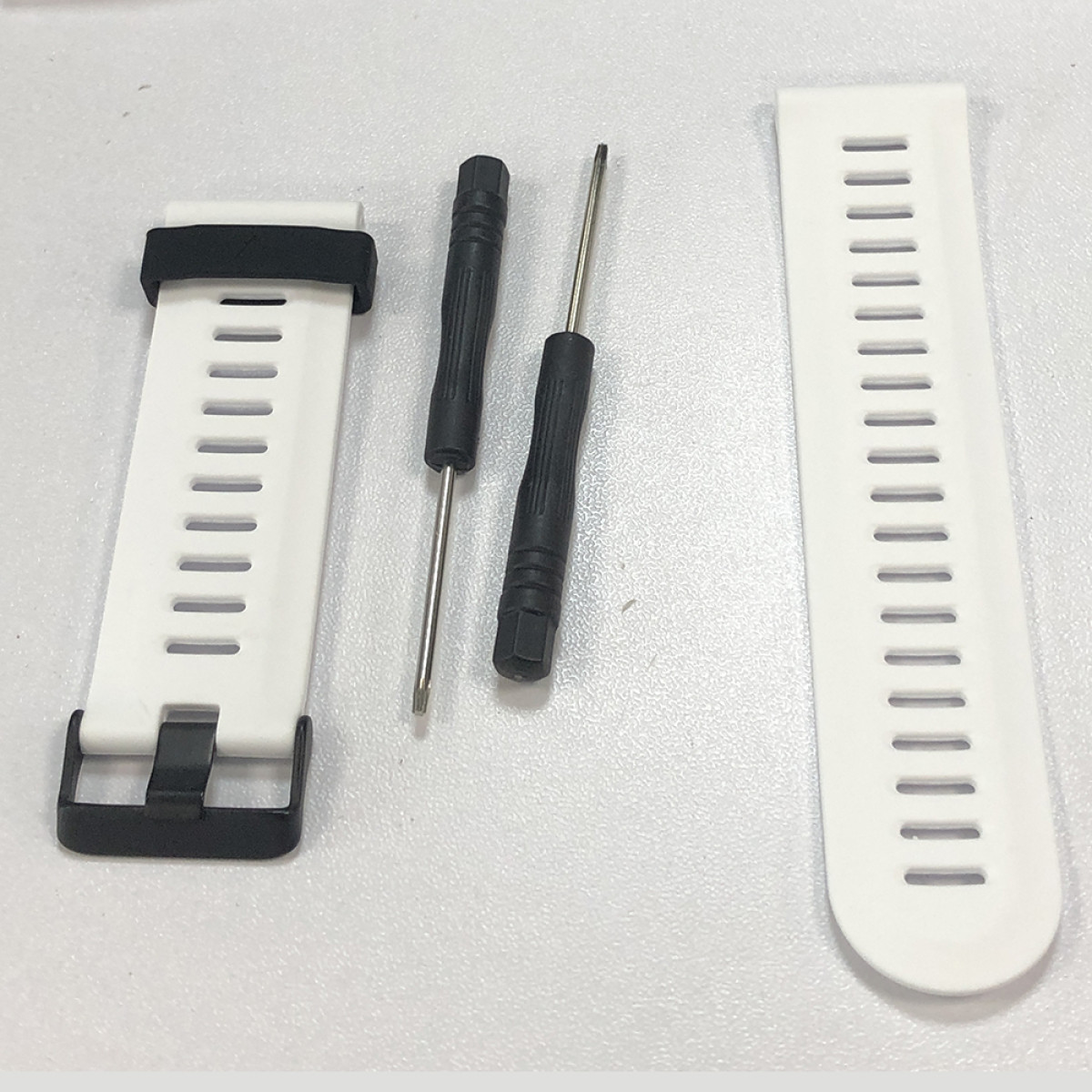 Białe paski do zegarków, czarne śrubokręty. Jeden pasek z klamrą, drugi z otworami. Śrubokręty mają czarne uchwyty i srebrne końcówki.