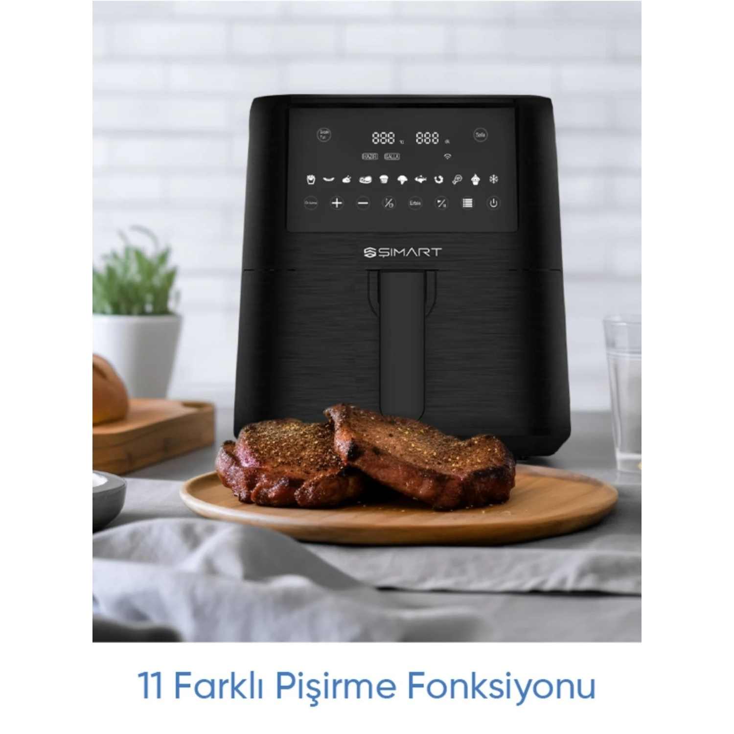 Ahşap tabakta pişmiş etli siyah bir hava fritözü. Arka planda bir bitki ve bir bardak. Metin '11 farklı pişirme fonksiyonu' diyor.