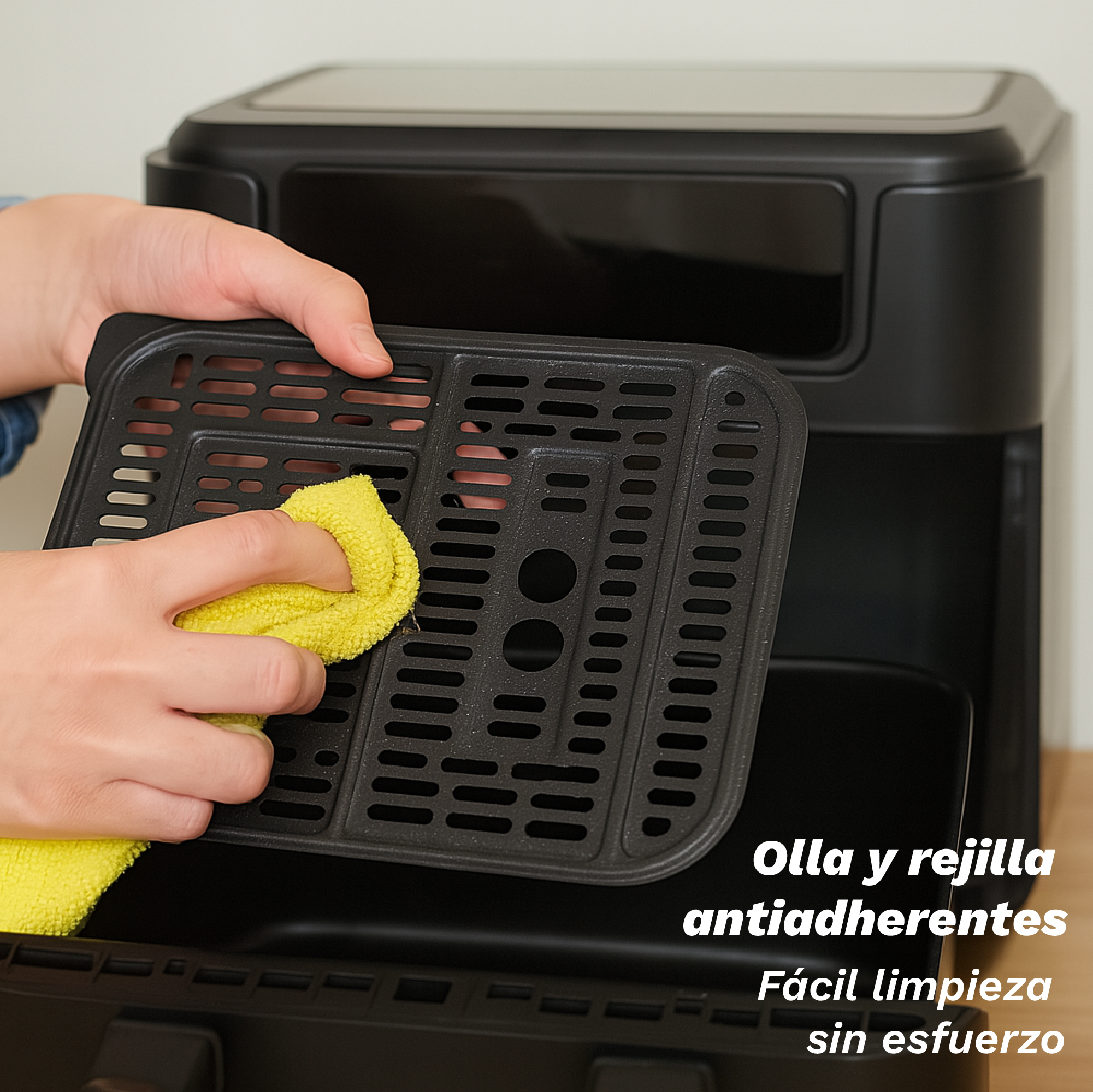 Una persona pulisce un vassoio nero per friggitrice ad aria con un panno giallo. La friggitrice è nera.