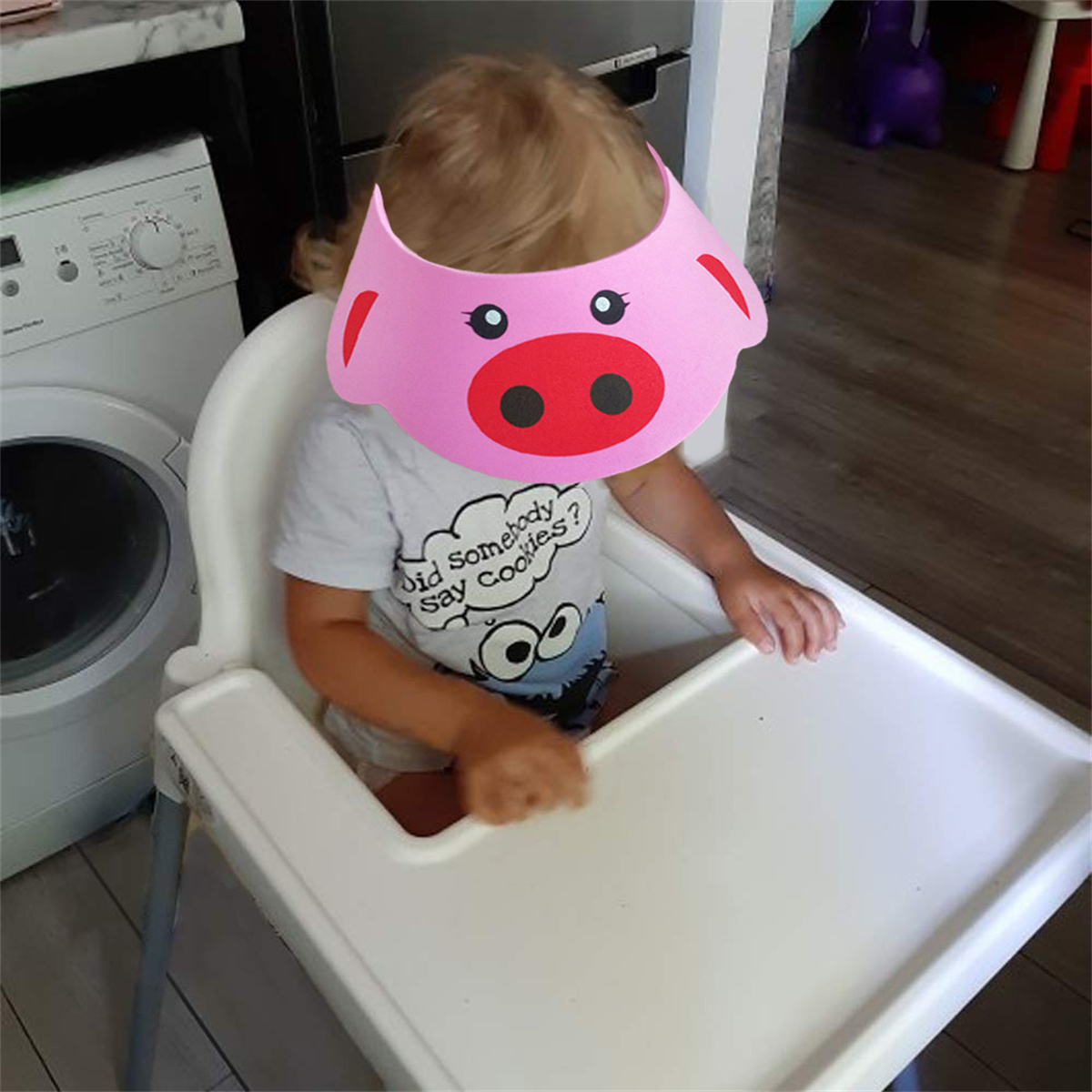 Ein Kind mit einem Schweinevisier sitzt in einem Hochstuhl. Das Kind trägt ein T-Shirt mit der Aufschrift 'Did somebody say cookies?'