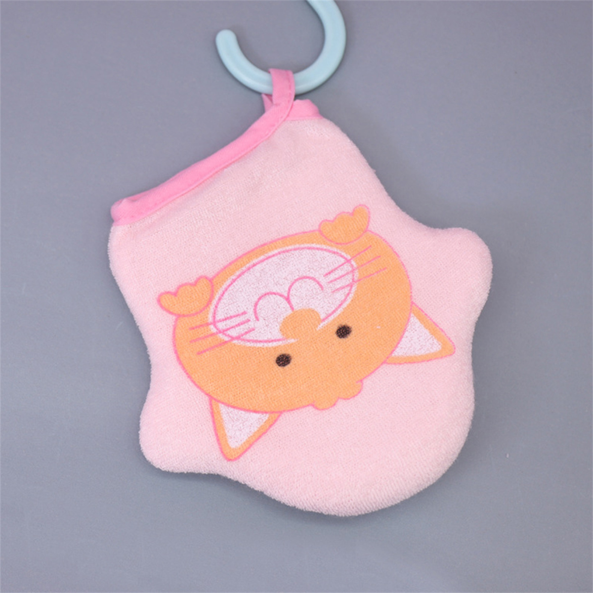 Ein rosa Waschlappen mit einem Katzen-Gesicht hängt. Er hat ein orangefarbenes Katzen-Gesicht und einen blauen Haken. Der Hintergrund ist grau.