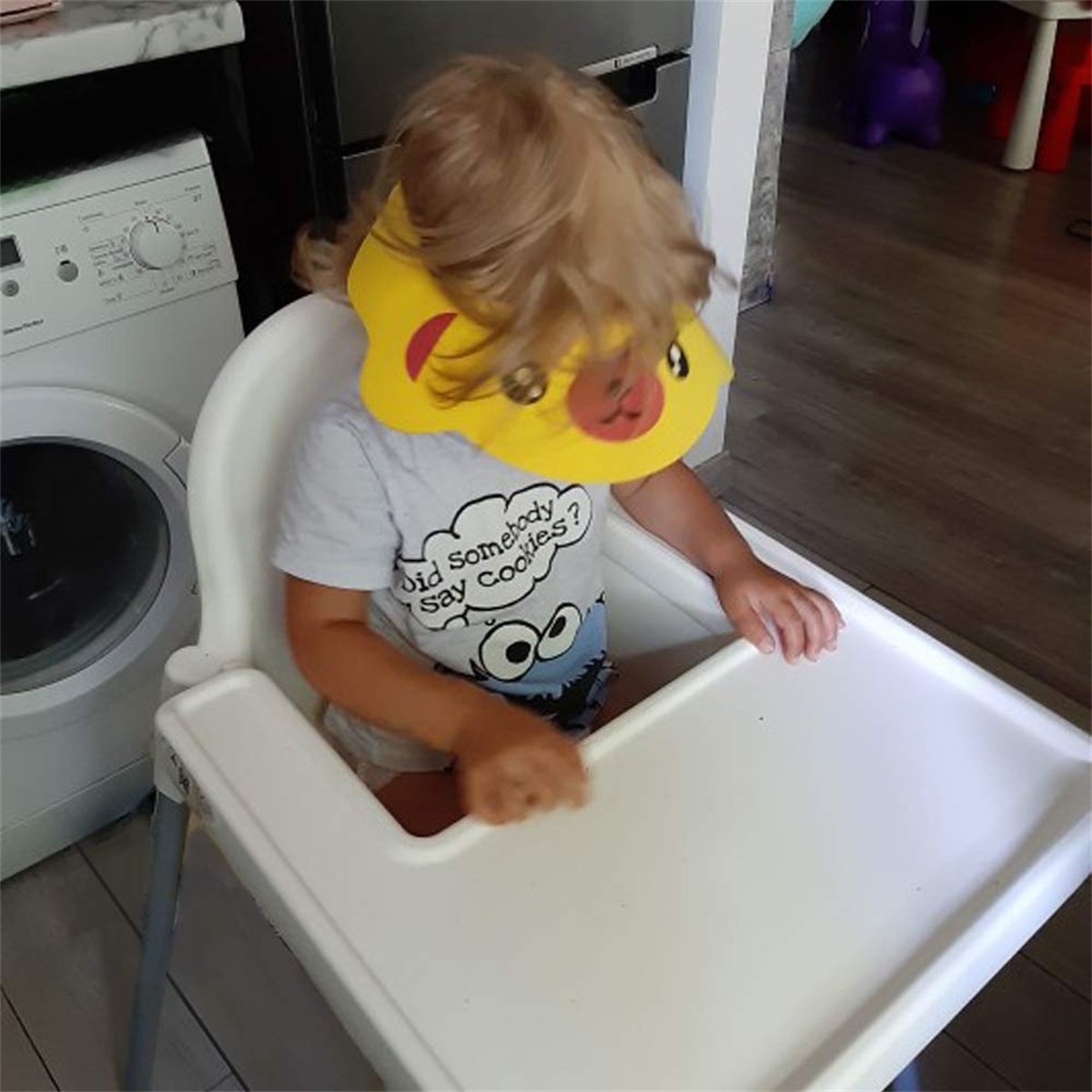 Ein Kind in einem Hochstuhl mit einem gelben Pikachu-Hut. Das Kind trägt ein T-Shirt mit der Aufschrift 'Hat jemand Kekse gesagt?'