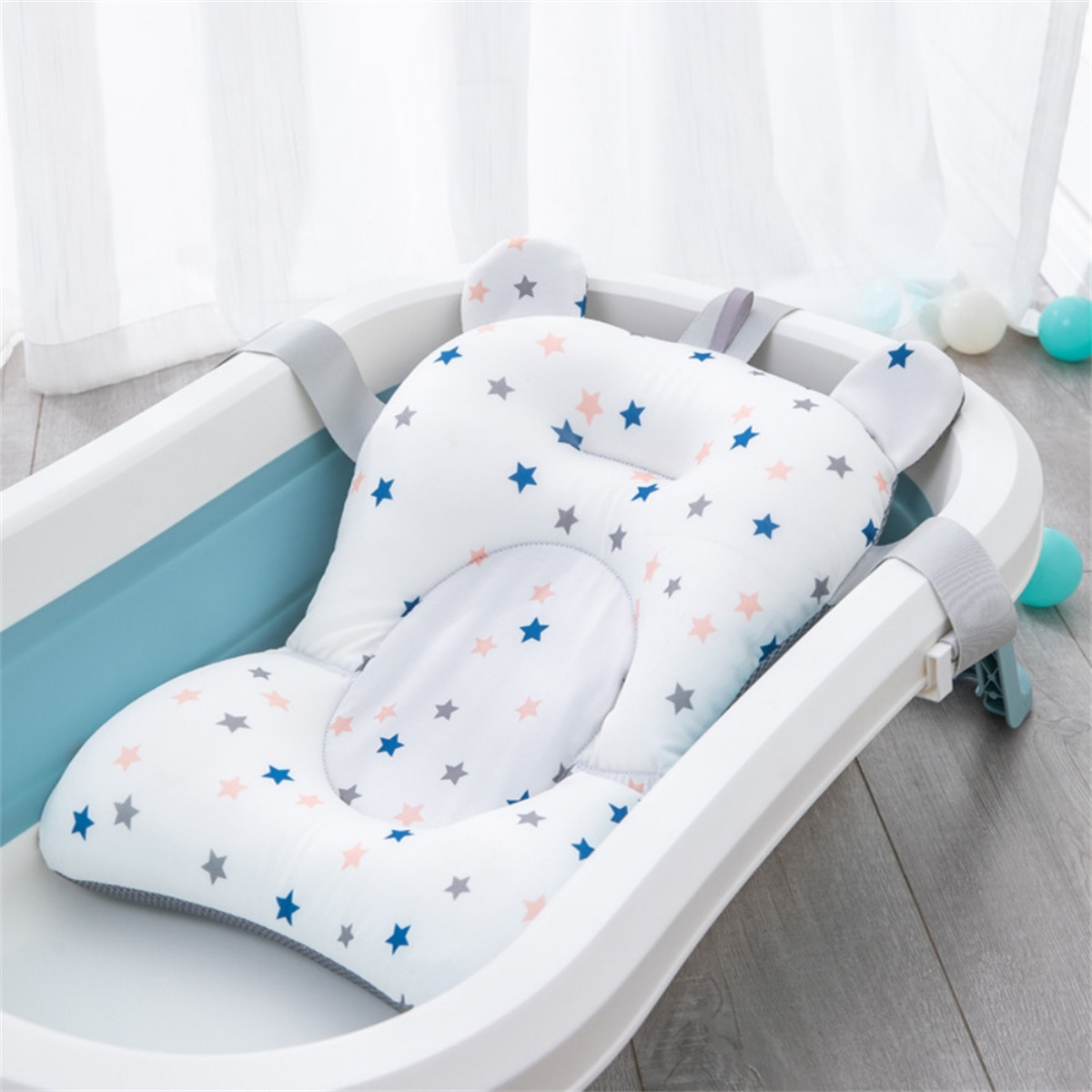 Ein Babybad mit einem sternförmigen Kissen. Das Bad ist hellblau und wei ß. Einige Bälle liegen auf dem Boden.