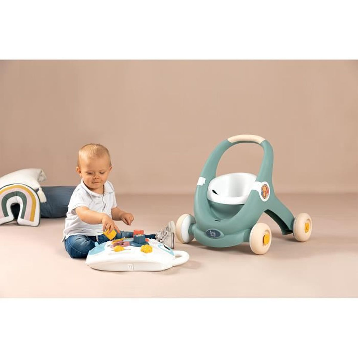 Ein Baby spielt mit Blöcken. Ein Lauflernwagen und Kissen sind in der Nähe. Die Szene ist drinnen.