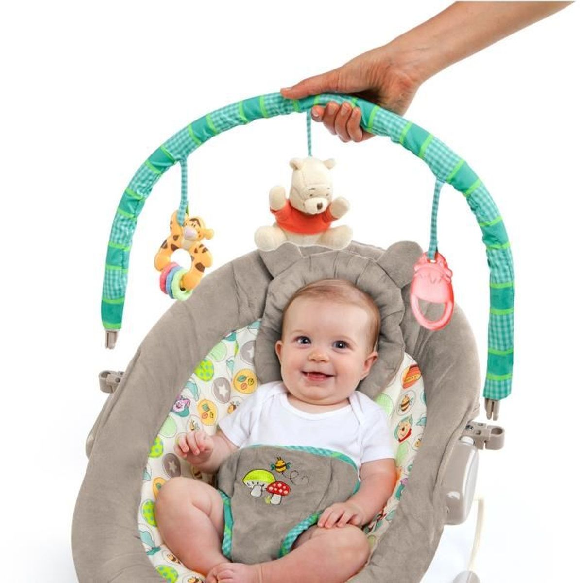 Ein Baby in einer grauen Babywippe lächelt. Spielzeug hängt darüber. Eine Hand hält den grünen Bügel.