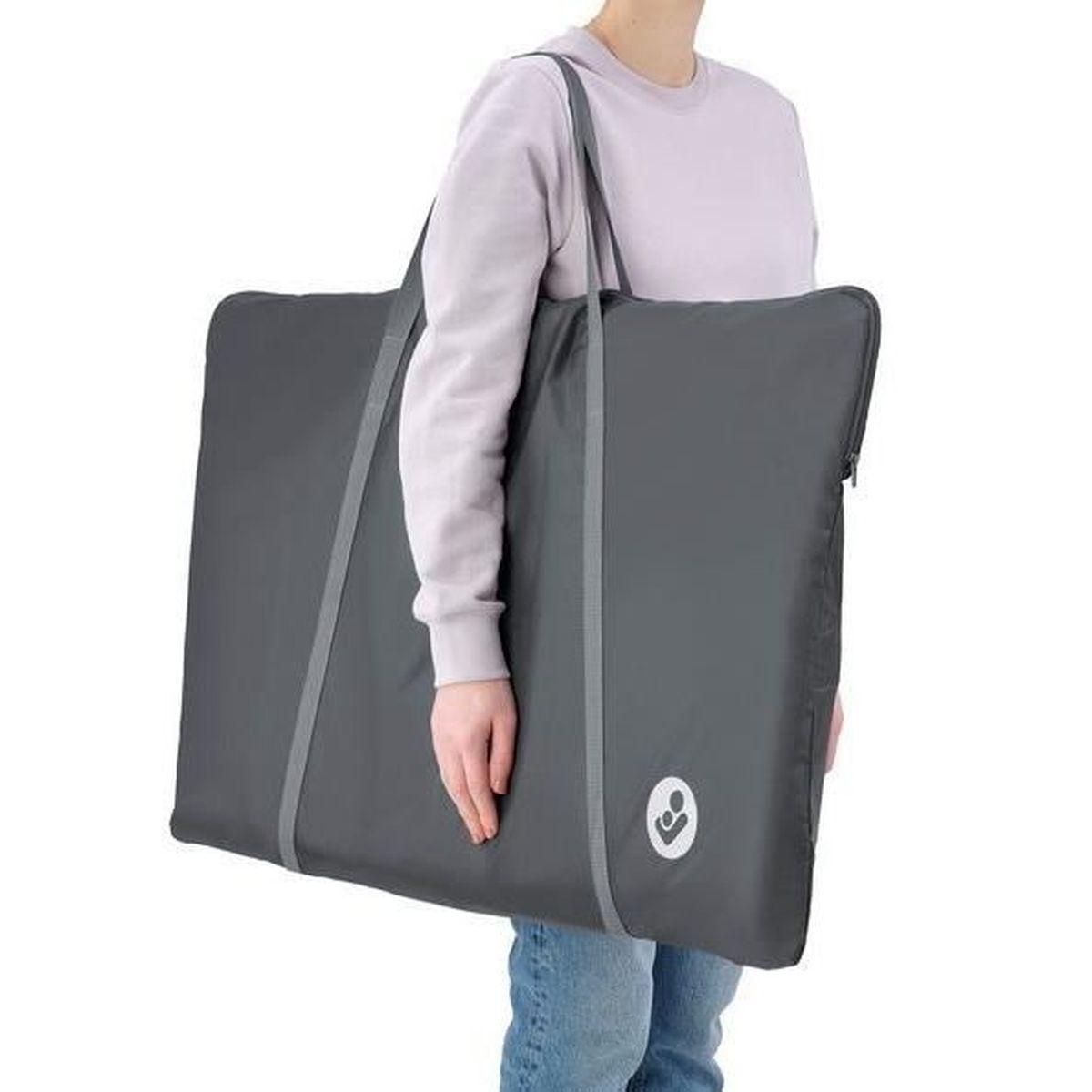 Eine Person trägt eine große, graue, rechteckige Tasche mit einem Logo. Die Person trägt Jeans und einen hellgrauen Sweatshirt.