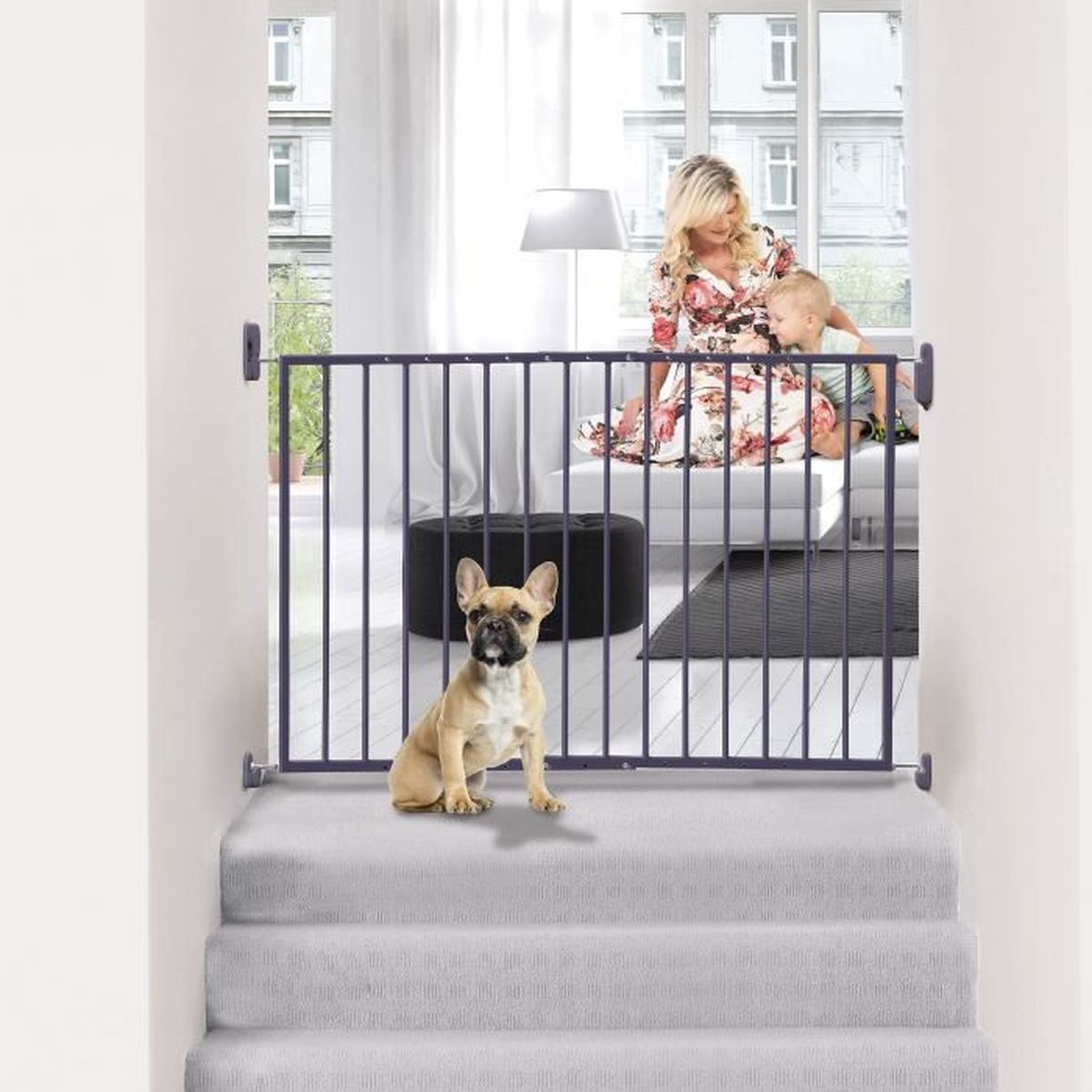 Ein Hund sitzt vor einem Gitter auf einer Treppe. Eine Frau und ein Kind sind hinter dem Gitter. Im Hintergrund eine Lampe, ein Teppich und ein Fenster.